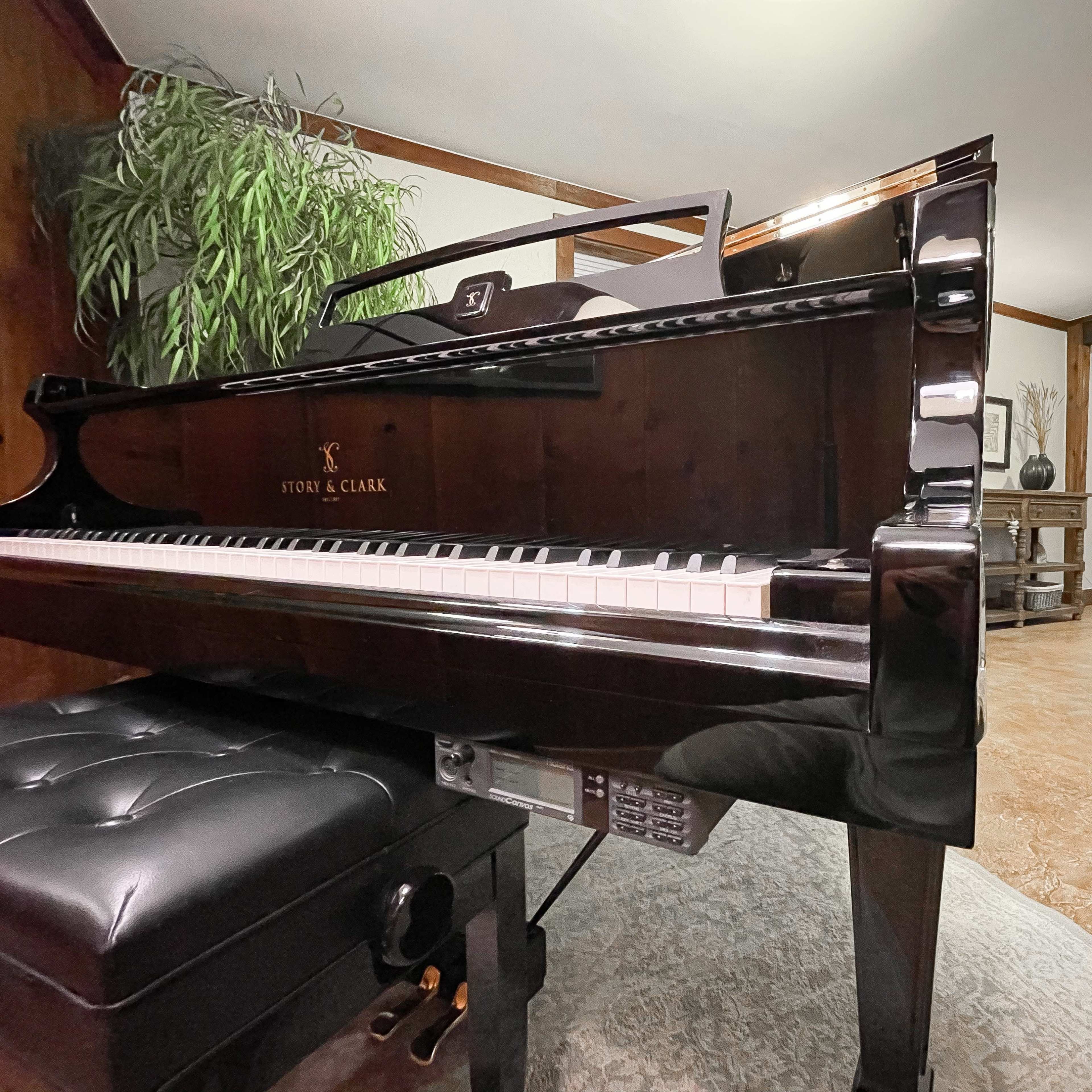 A black grand piano is positioned in a spacious room with wooden paneling and visible seating areas in the background.