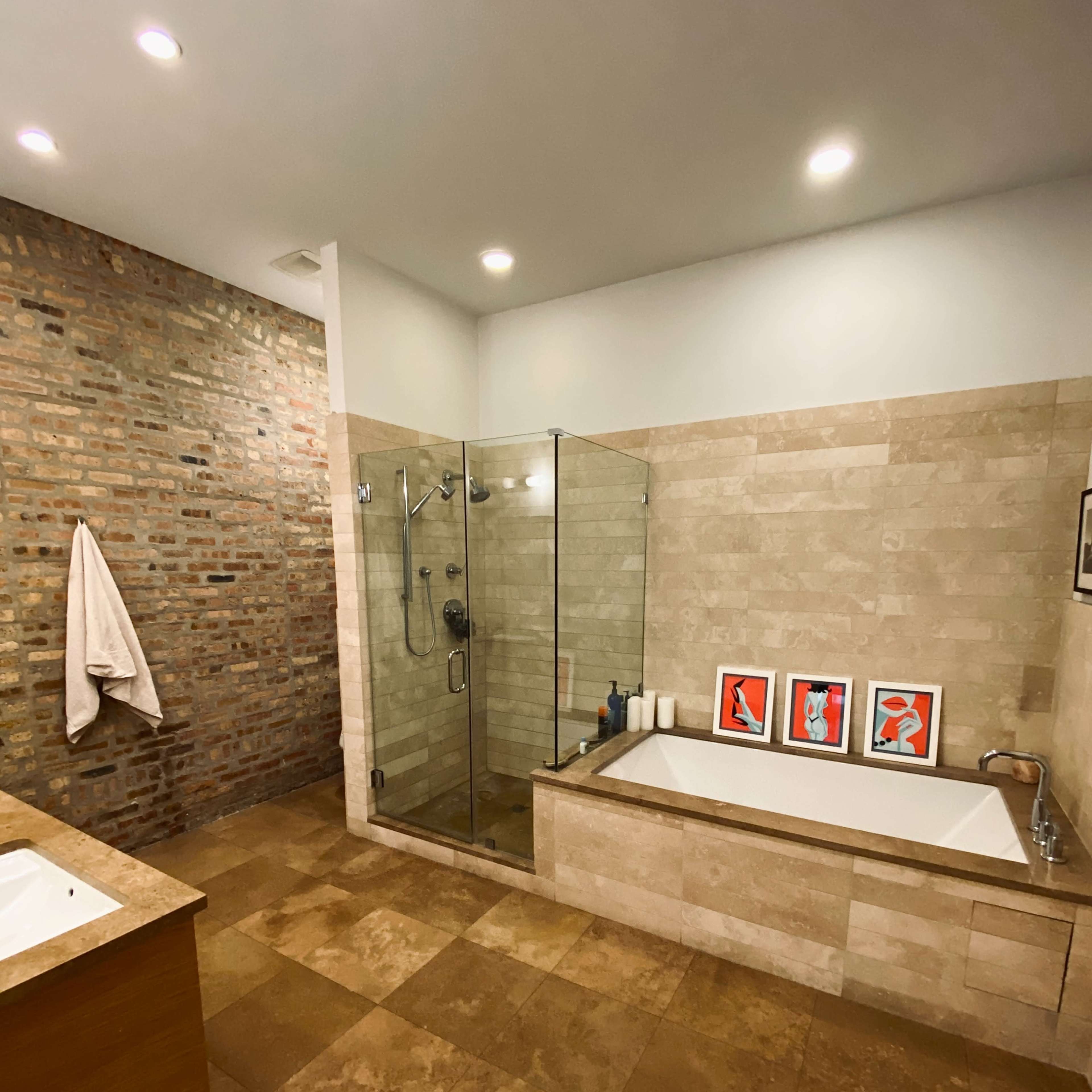 A modern bathroom featuring a glass shower enclosure, a bathtub, and a brick accent wall.
