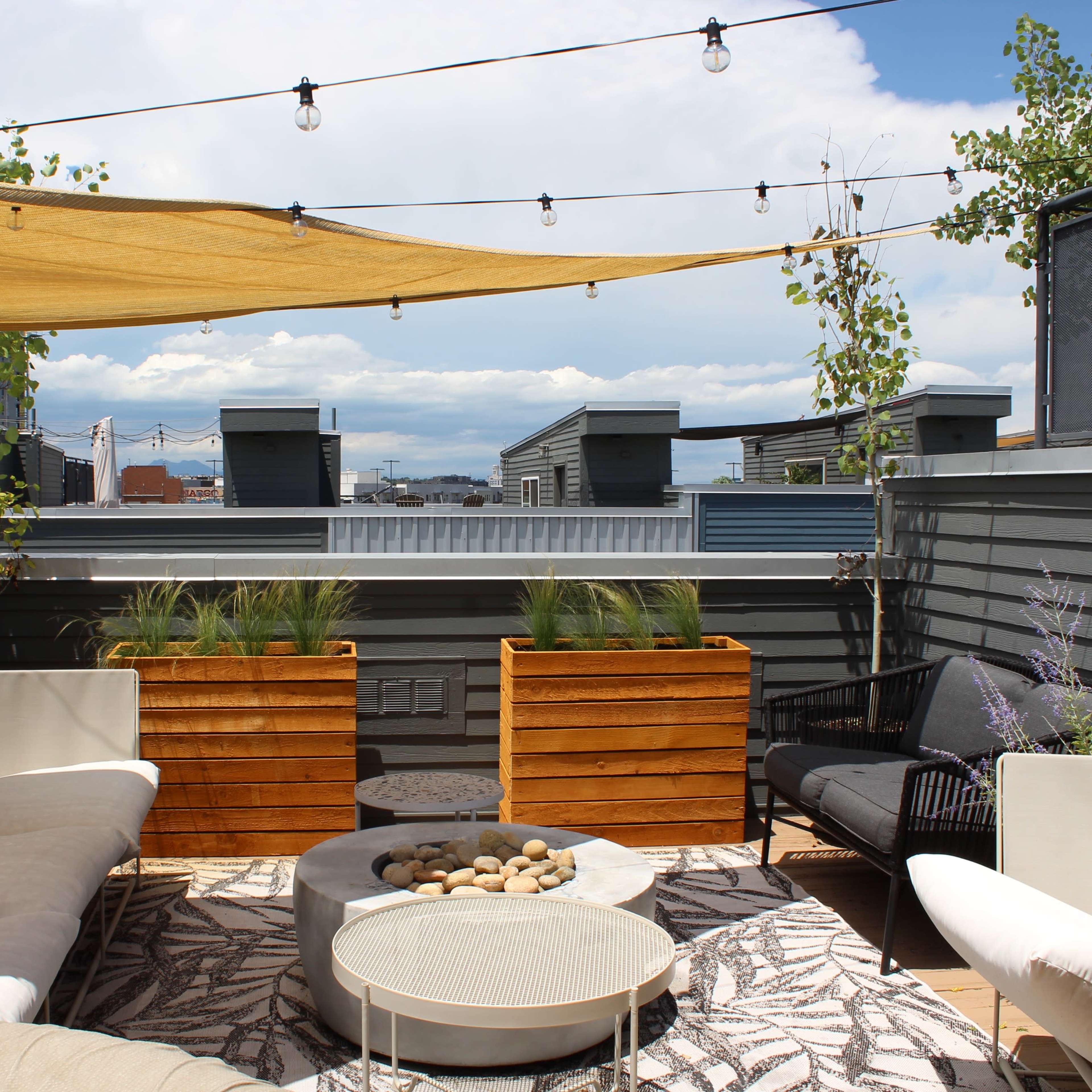 A rooftop patio featuring comfortable seating, decorative planters, and string lights under a canopy.
