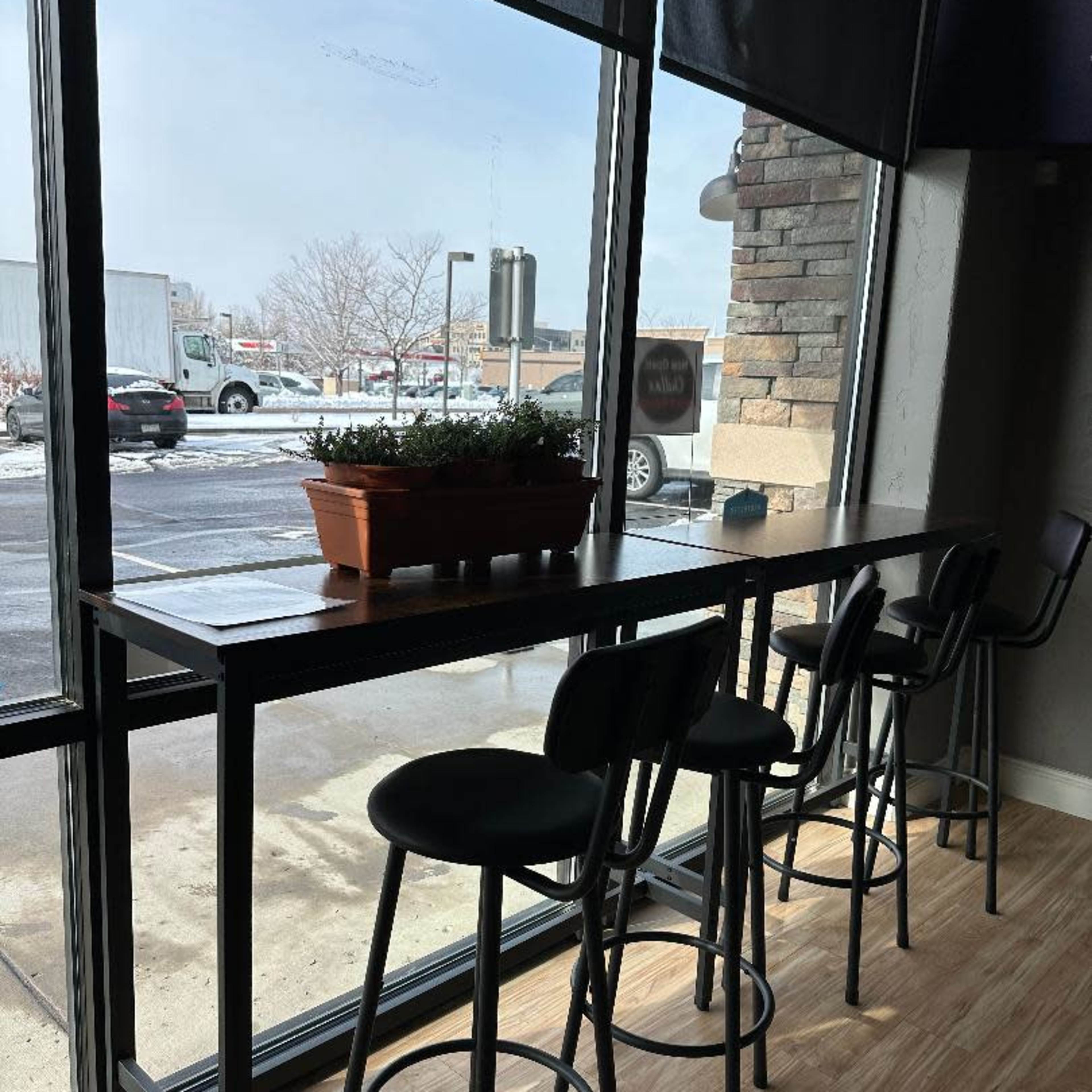 A long table with bar stools is positioned by large windows, overlooking a snowy outdoor scene.