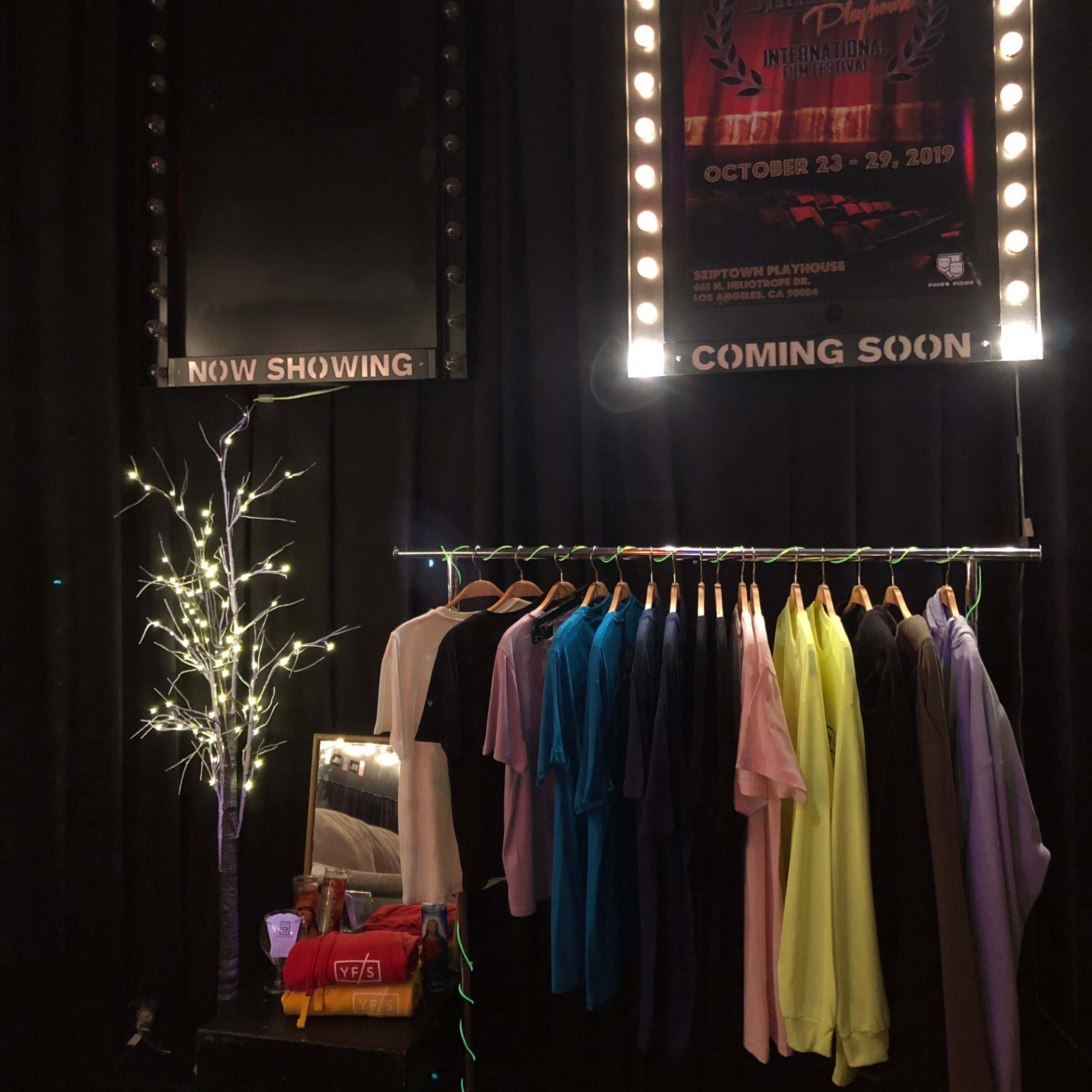A display area with clothing hanging on a rack, illuminated by lights, alongside posters for an event.