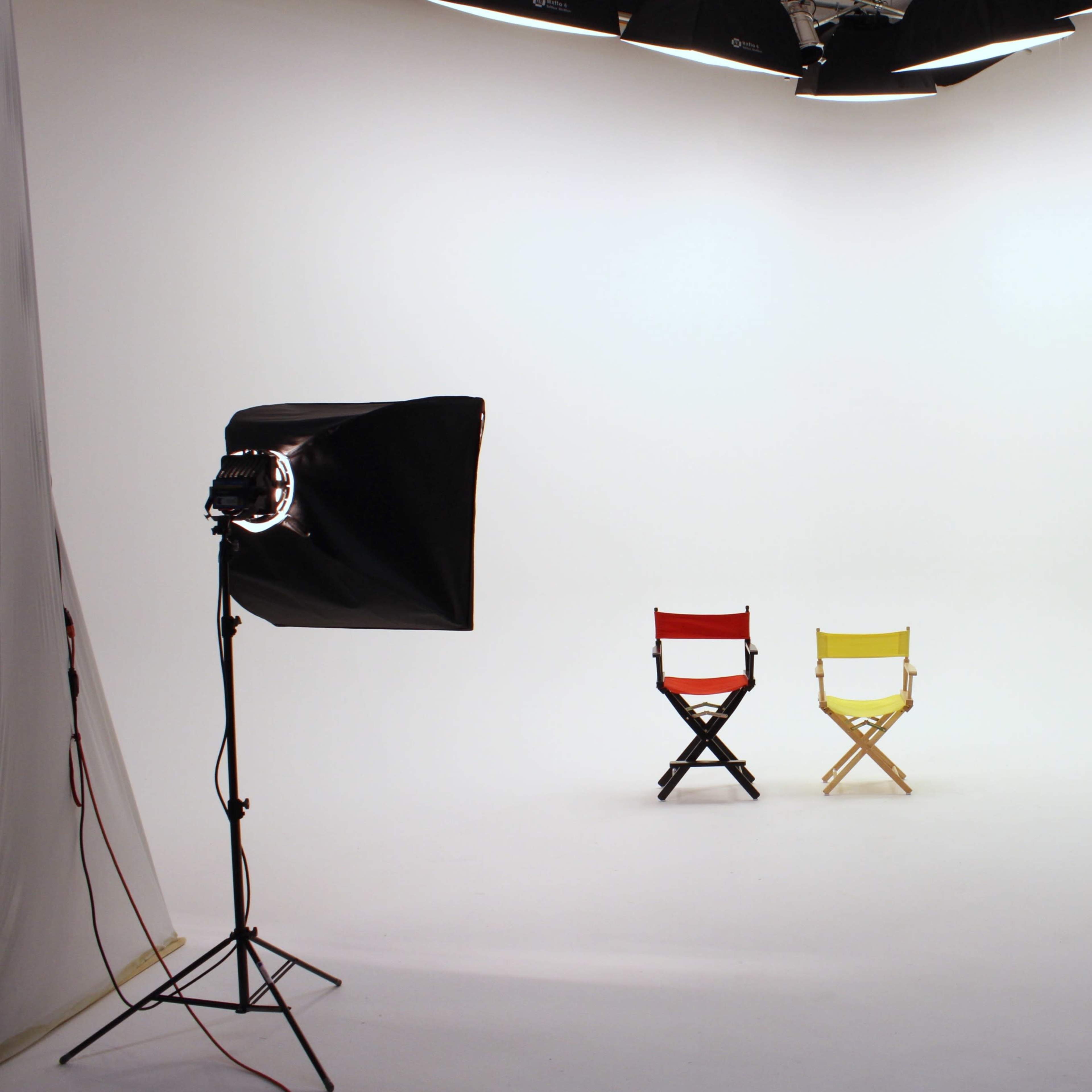 A minimalist photography studio featuring two director's chairs, one red and one yellow, under soft lighting.