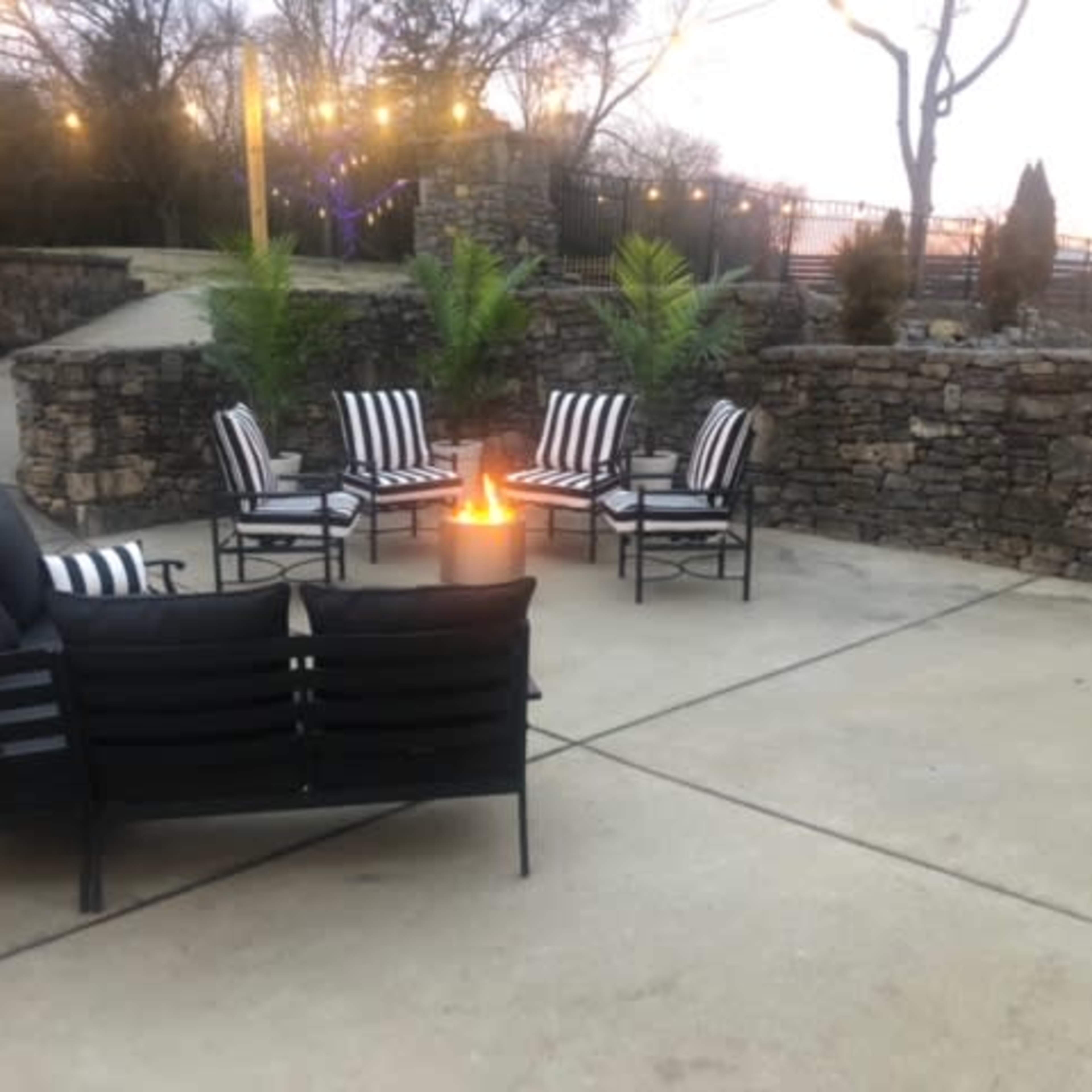 A circular seating area with black and white striped chairs surrounding a fire pit is set against a stone wall in an outdoor patio space.