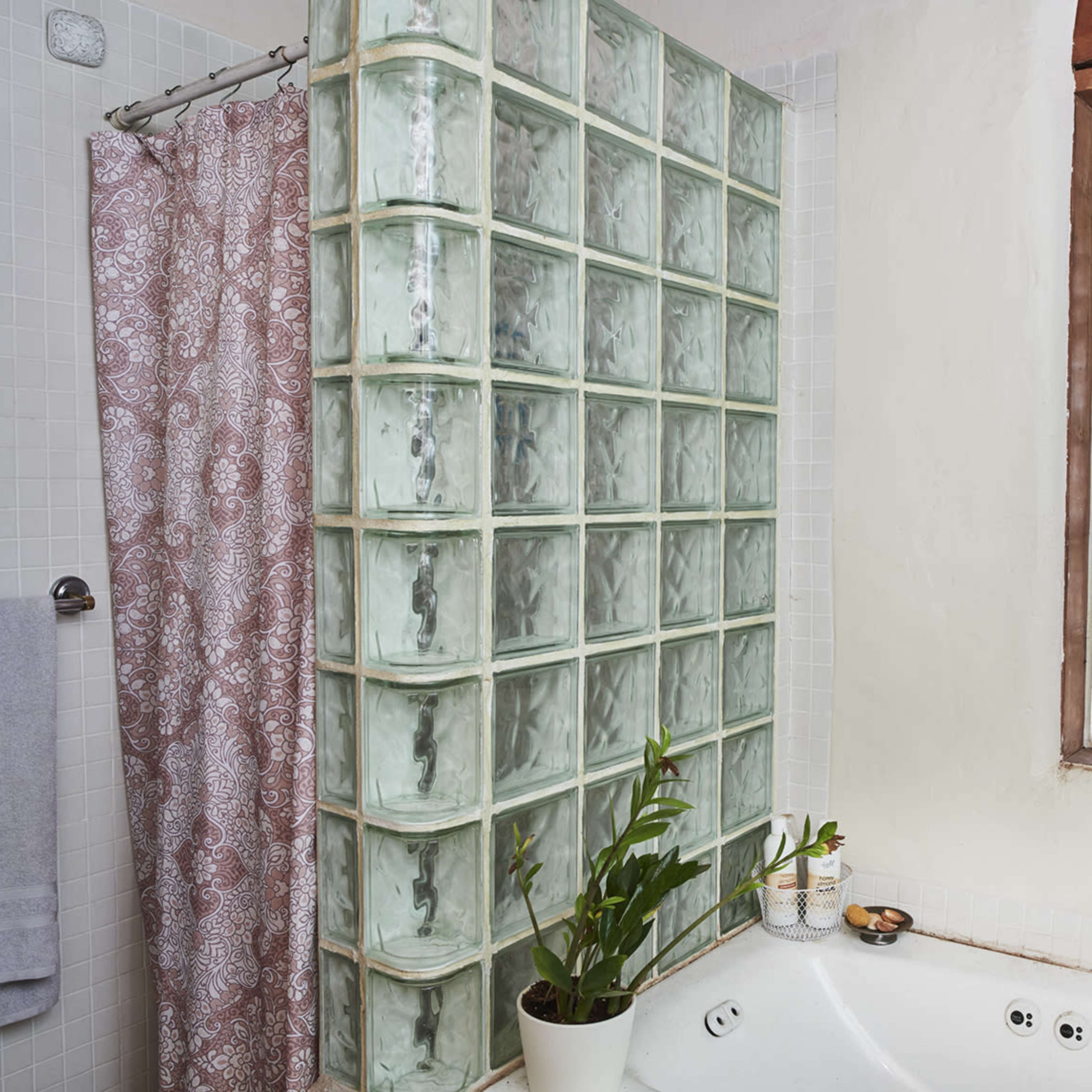 A bathroom with a glass block shower wall, a bathtub, and a window featuring frosted glass panes.