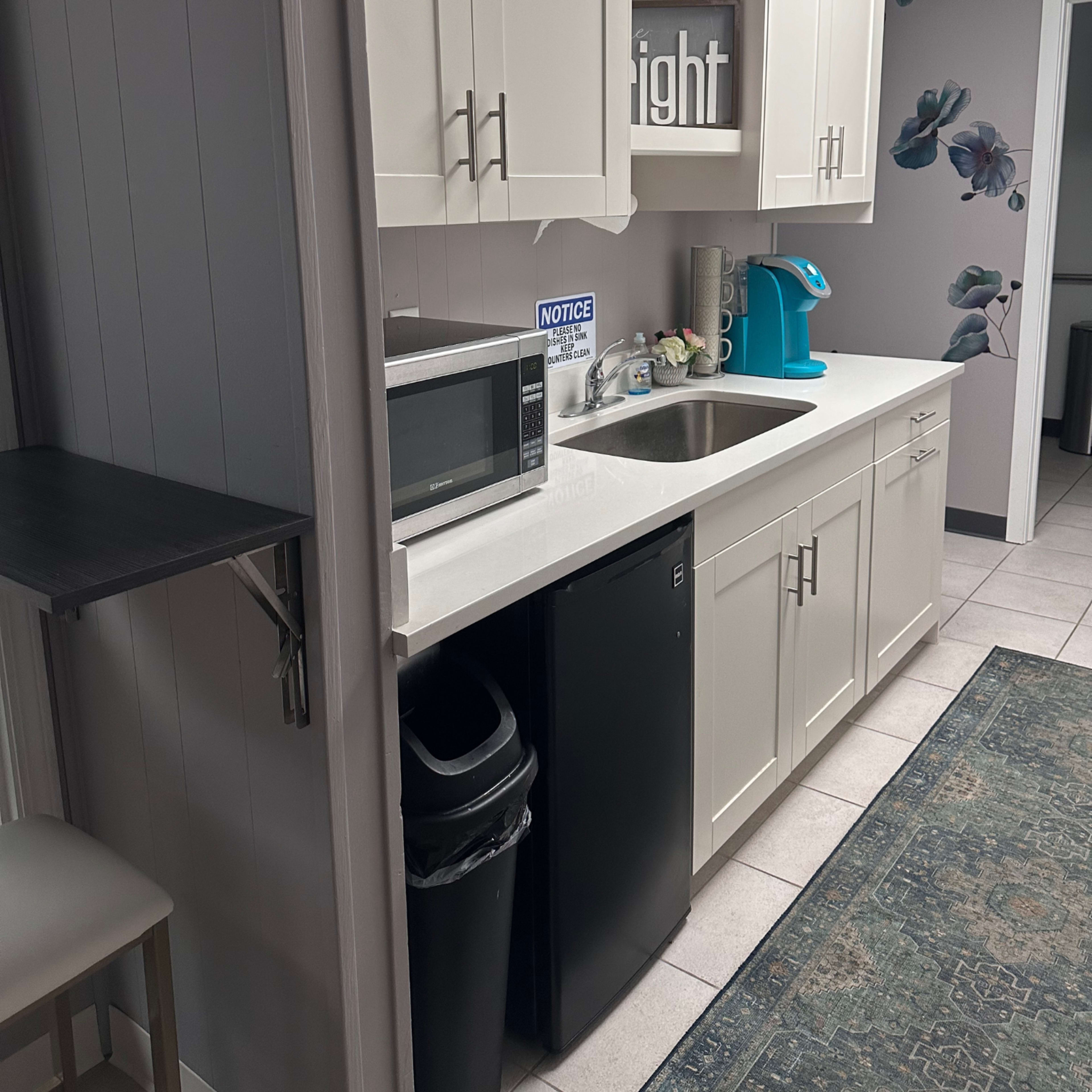 A modern kitchen with white cabinets, a sink, a microwave, a black refrigerator, and a teal coffee maker.