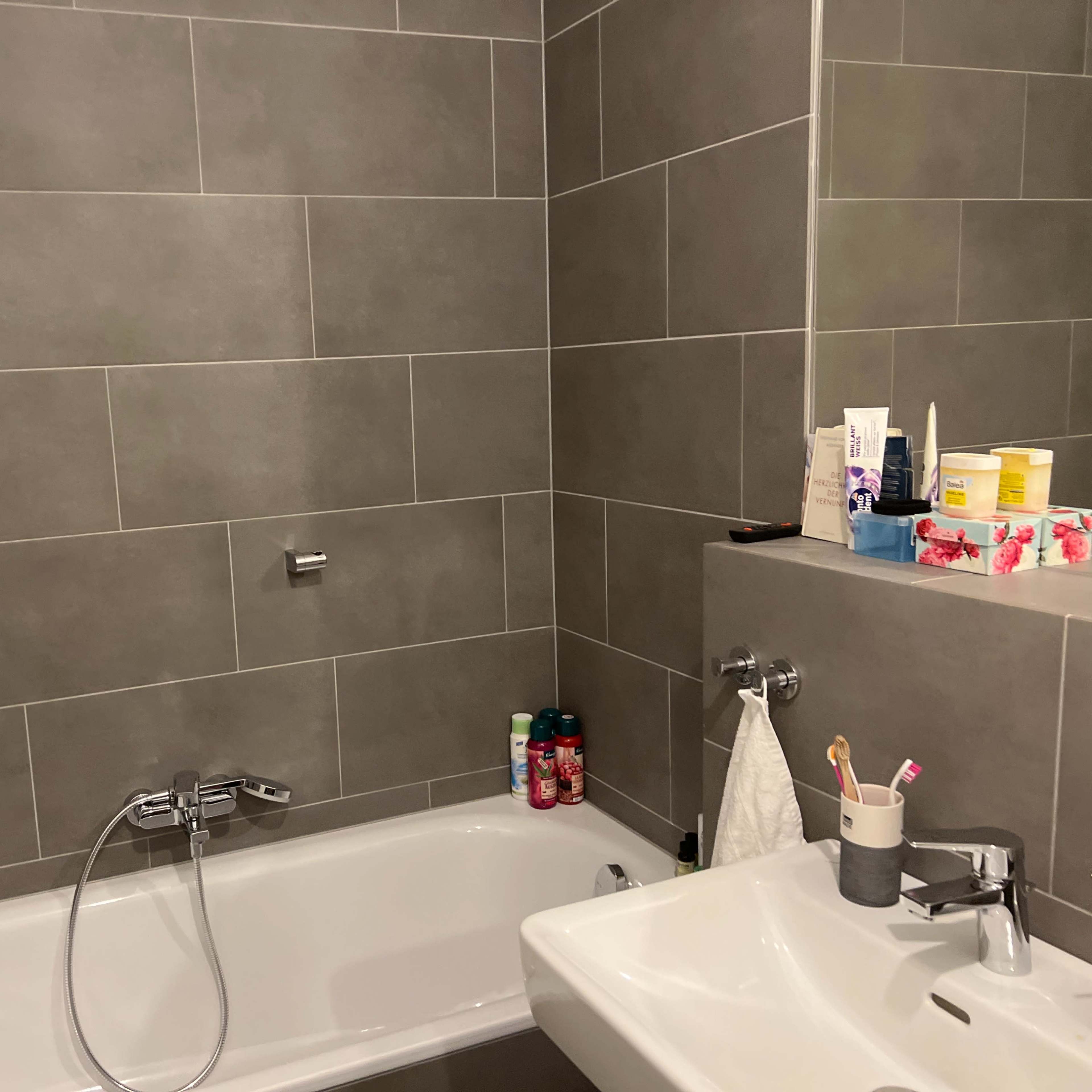 A modern bathroom featuring a bathtub, a sink with a mirror, and gray tiled walls.