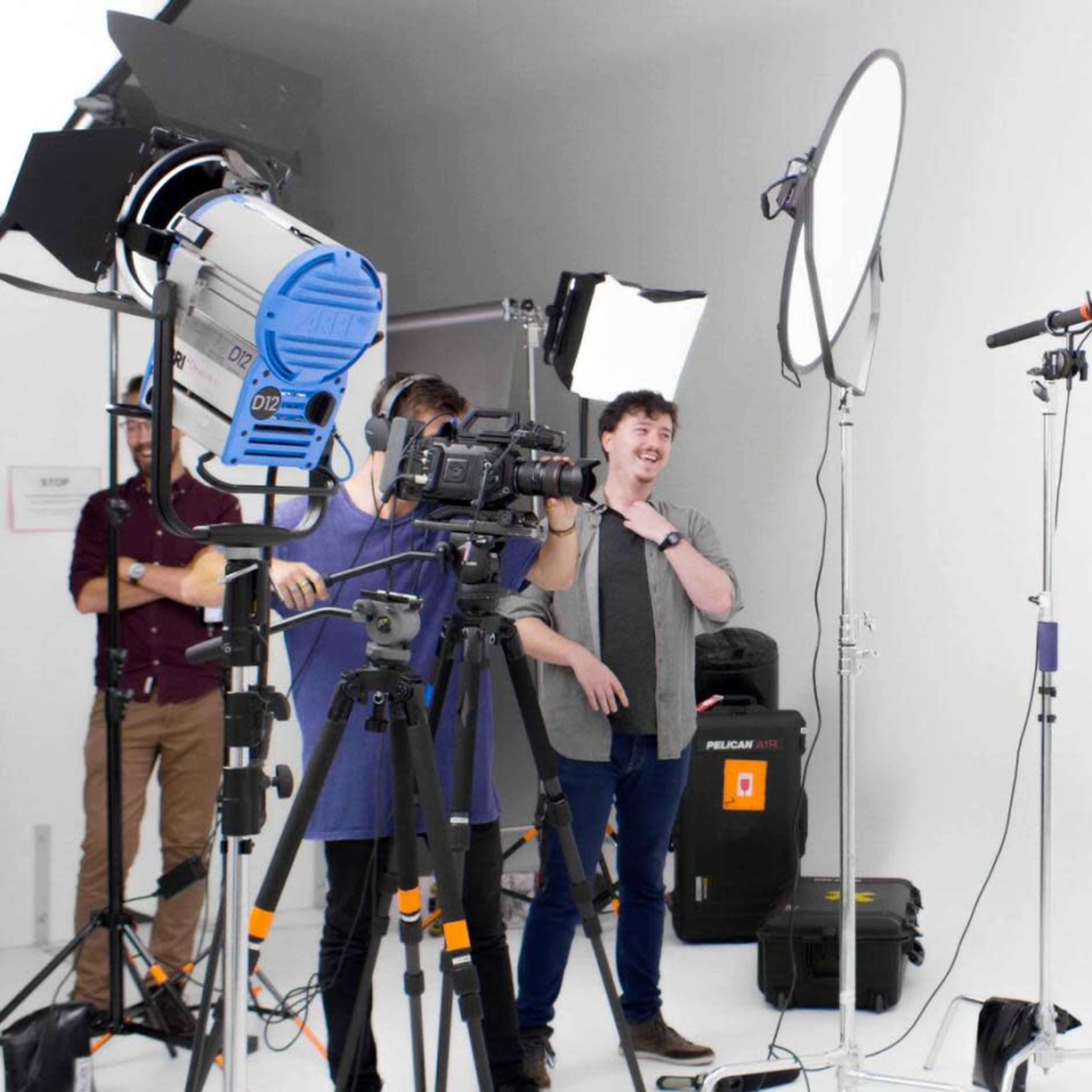 A film crew sets up equipment, including cameras and lights, in a bright studio to shoot a segment featuring a woman.