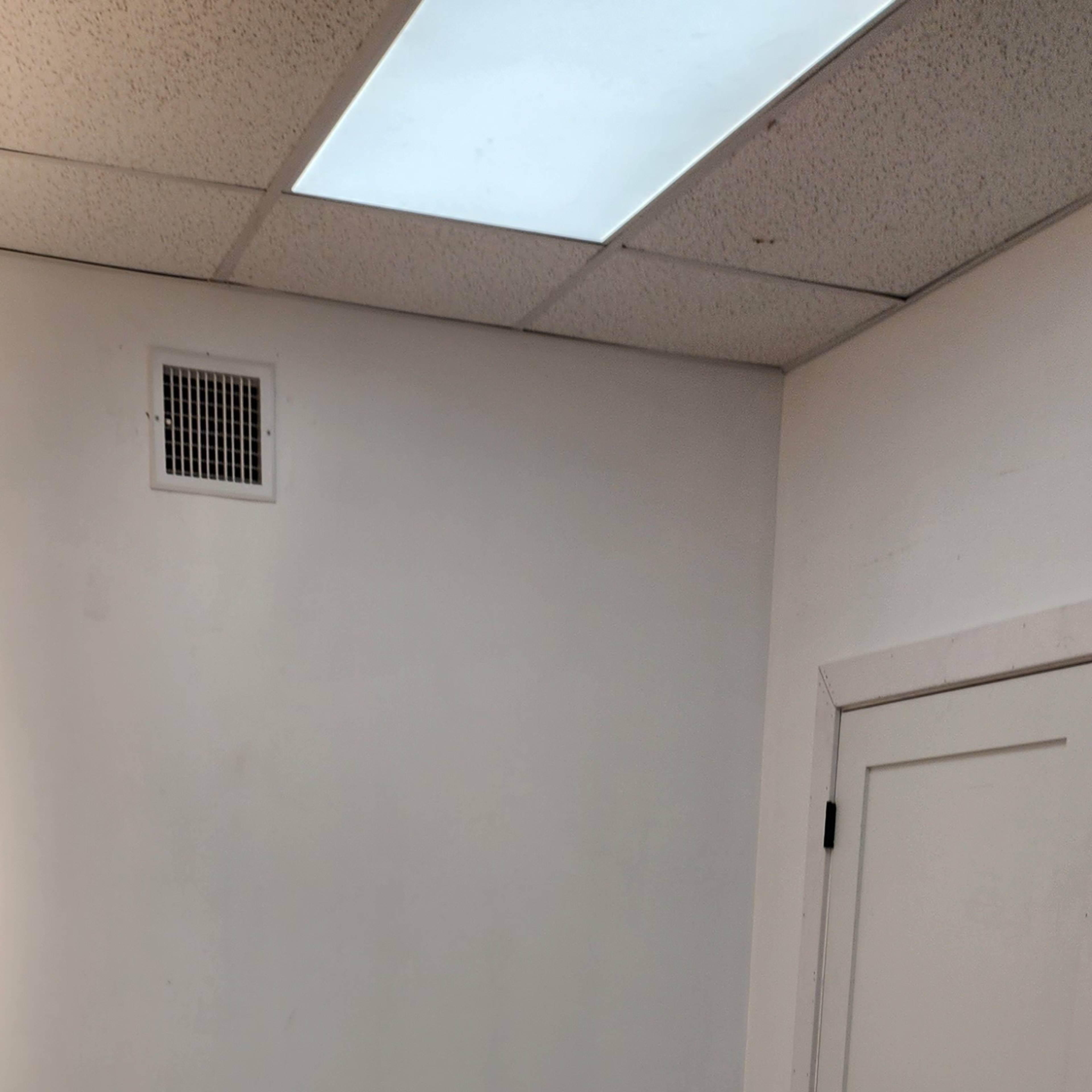 A sparsely furnished room with a textured floor, a white table on the left, and a closed door on the right.