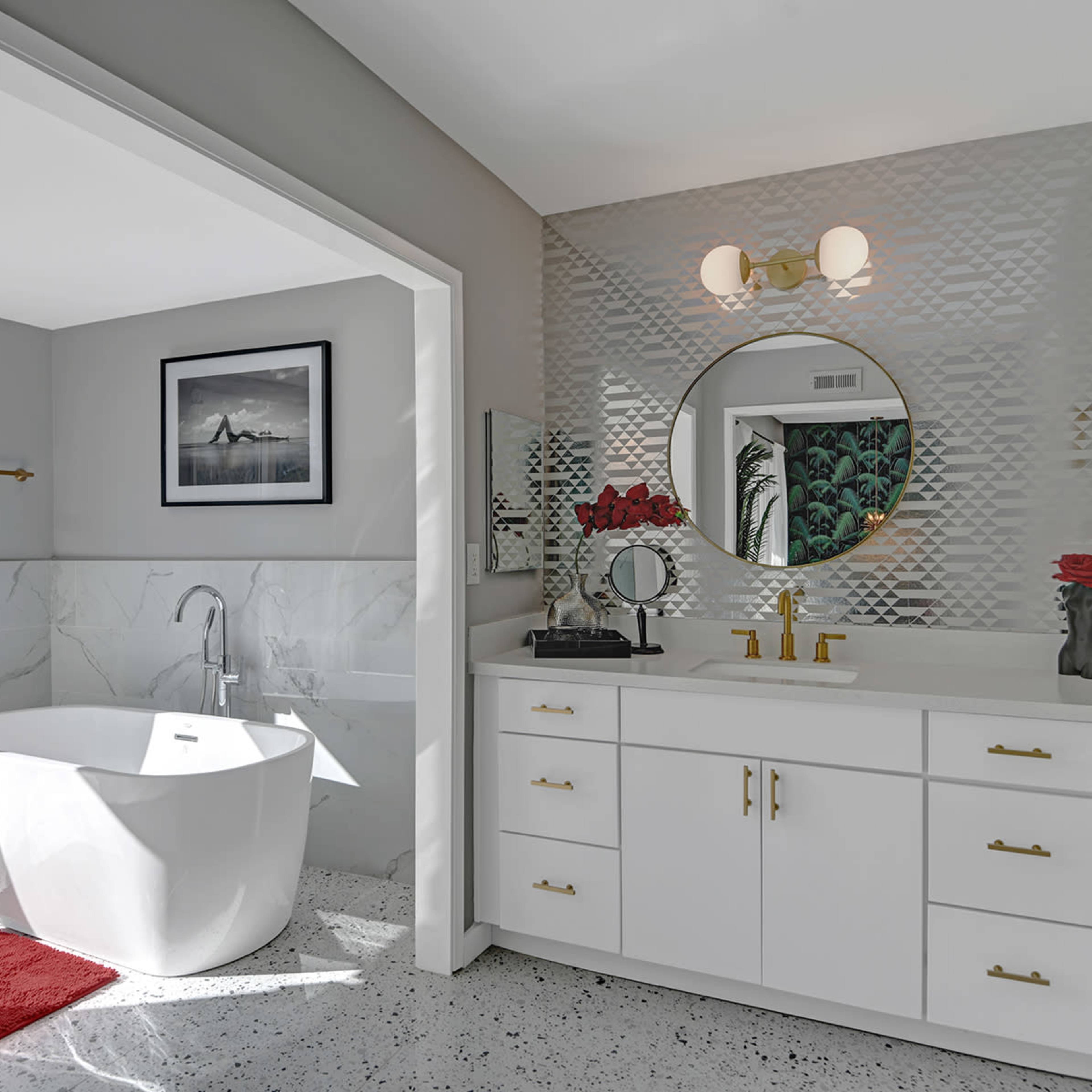 A modern bathroom features a freestanding tub, a double vanity with gold fixtures, and a textured wall behind the sink.