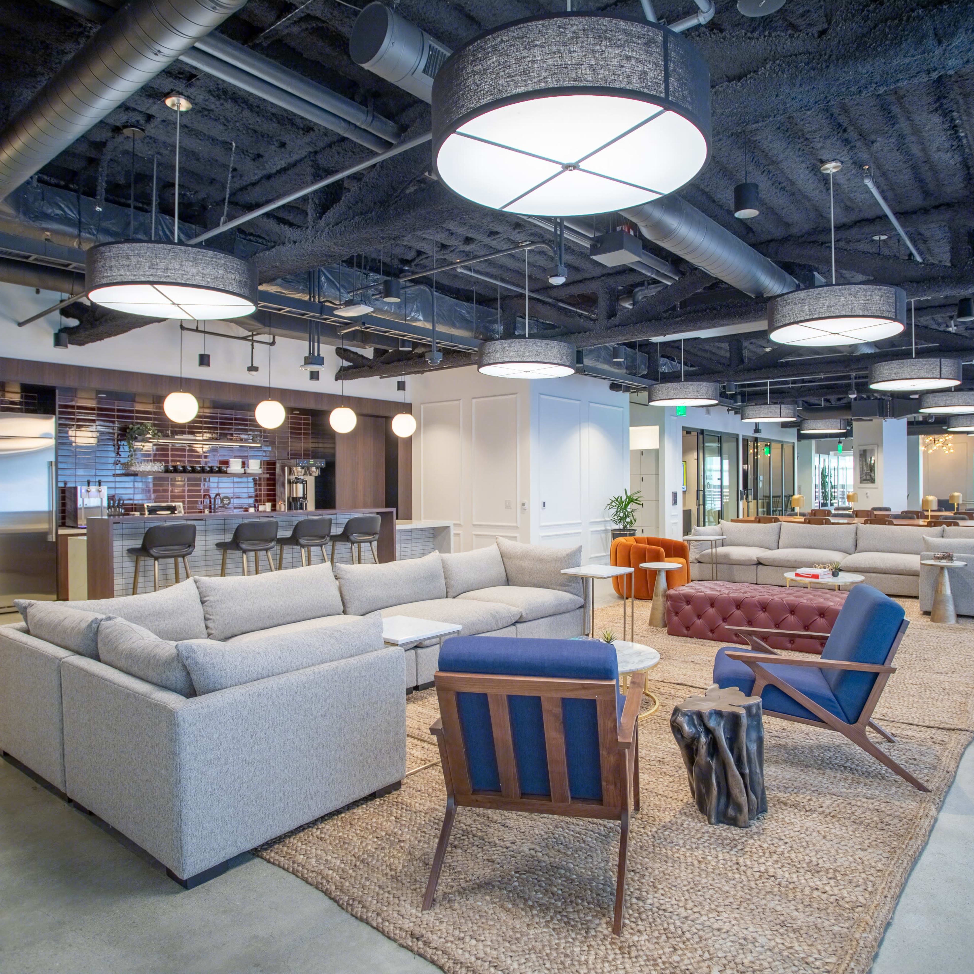 A modern office lounge area with gray sofas, a brown tufted chair, and round pendant lights hanging from the ceiling.