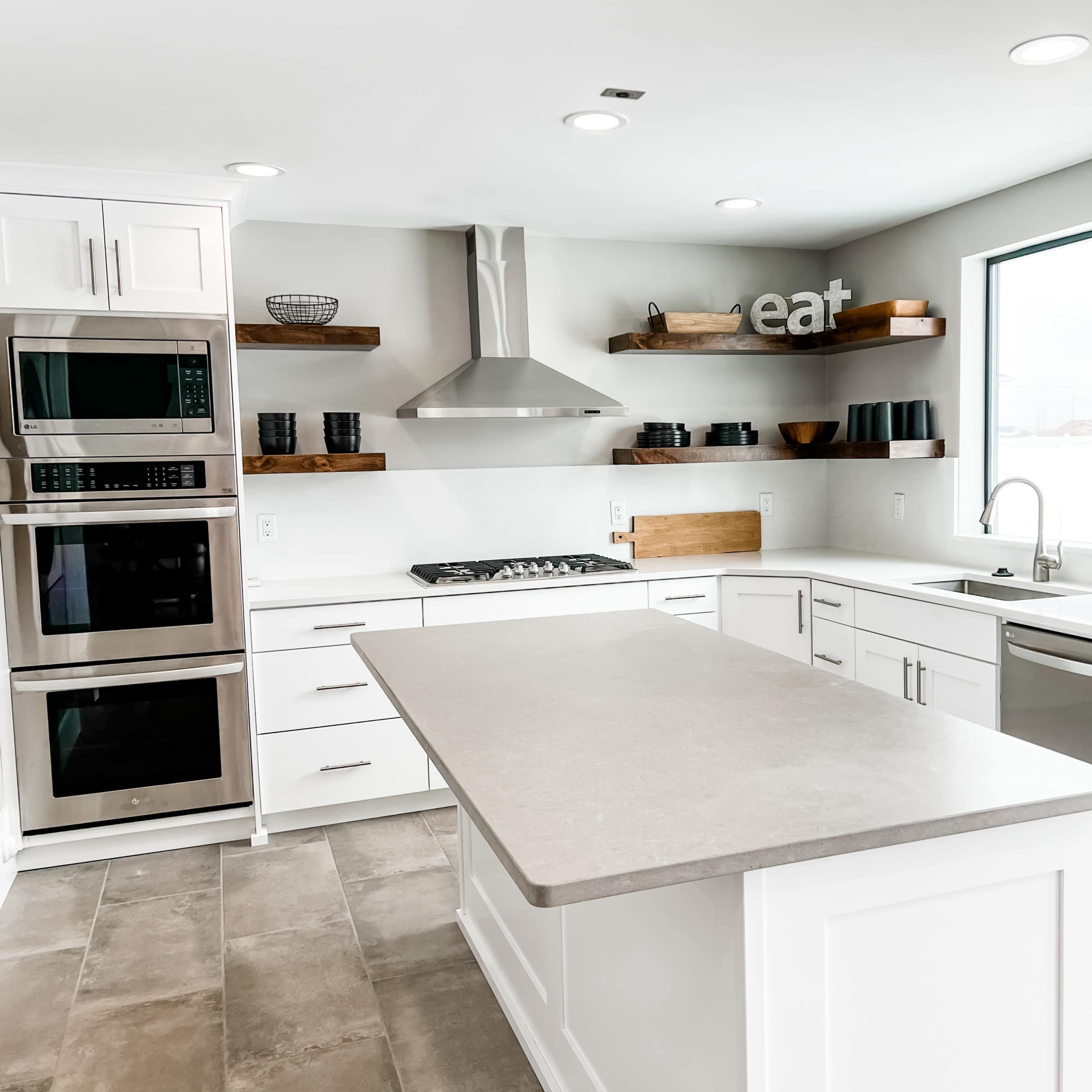 A modern kitchen features stainless steel appliances, white cabinetry, and a central island with a gray countertop.
