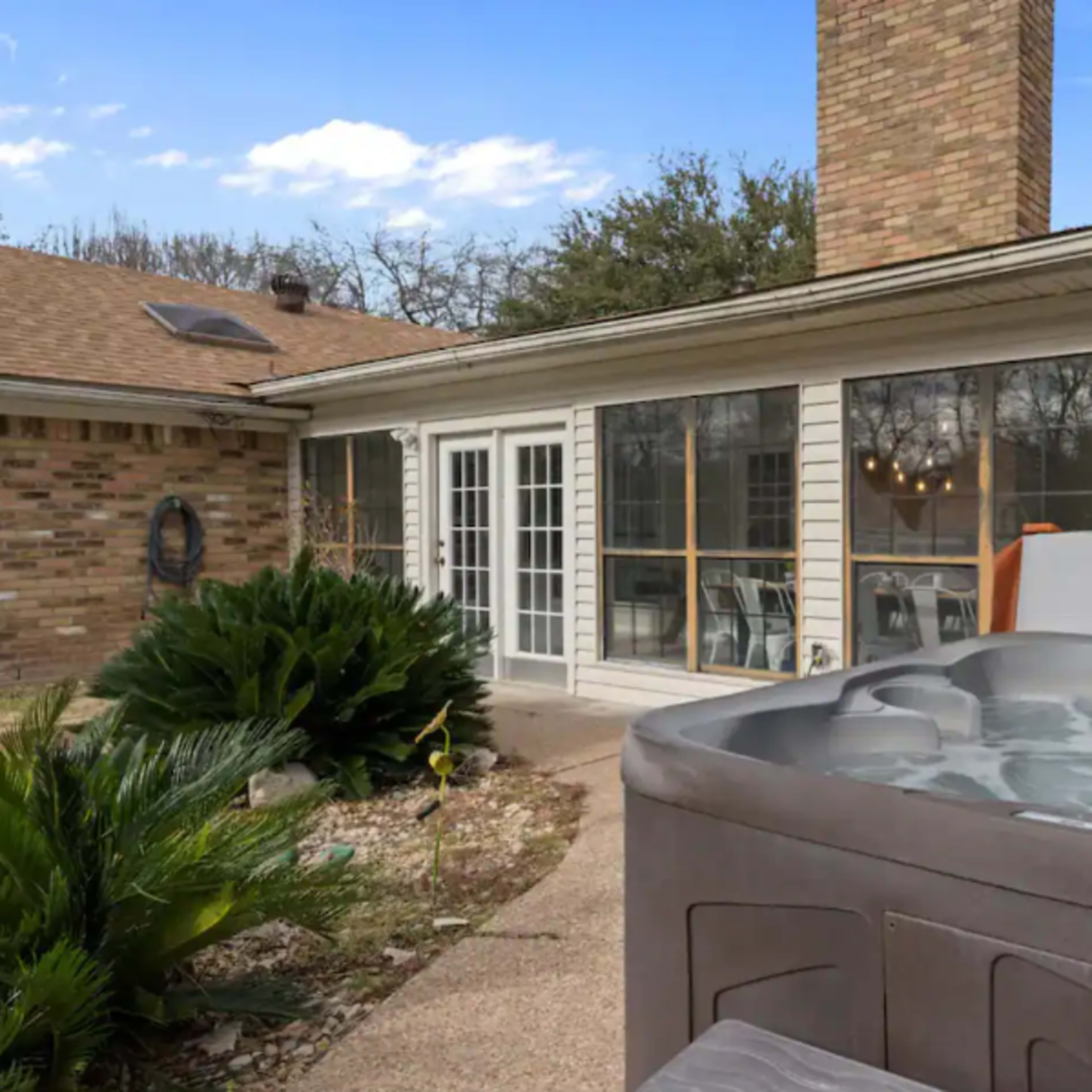A hot tub sits in the foreground of a patio area adjacent to a house with large glass doors and a brick exterior.