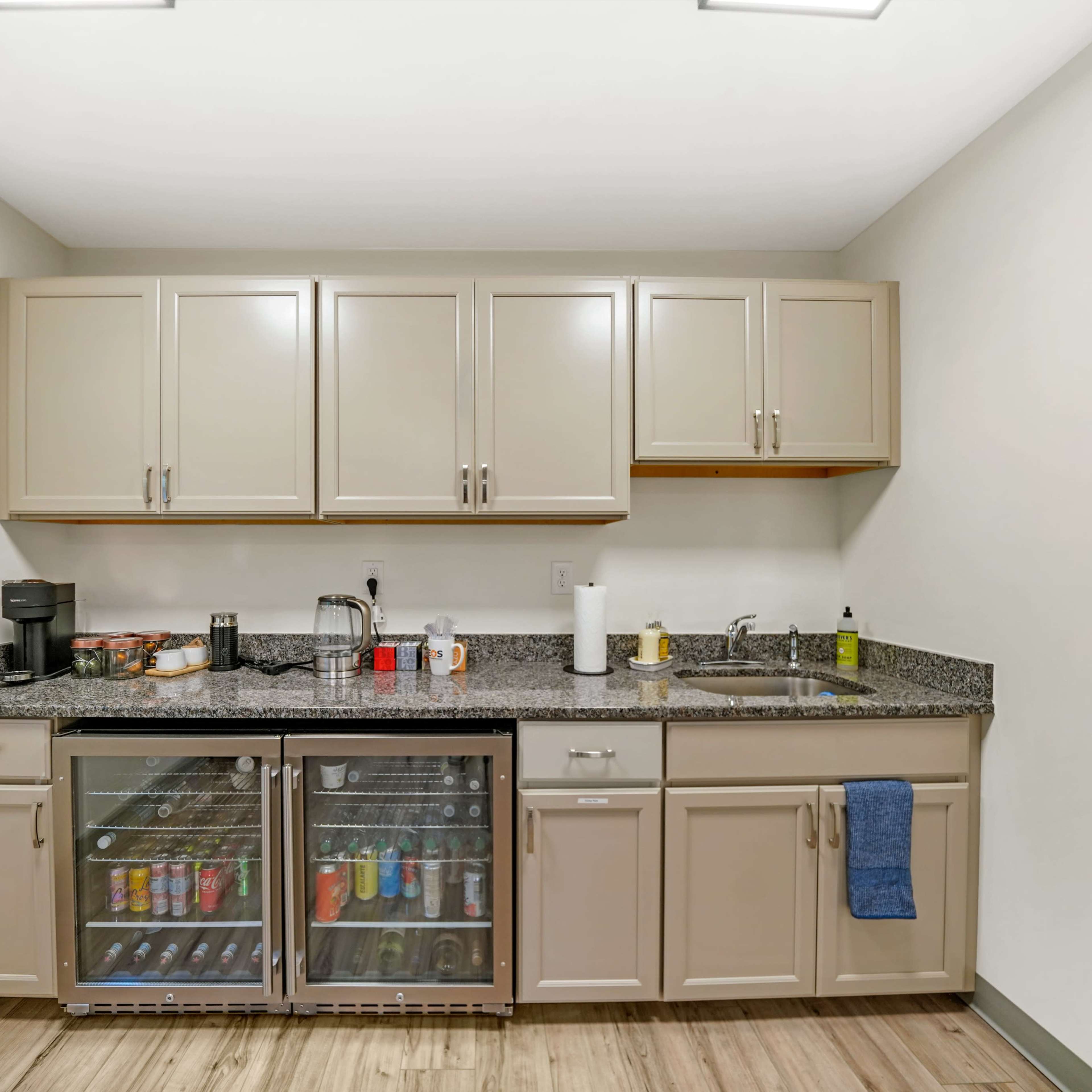 A modern kitchen with beige cabinets, a granite countertop, and an under-counter beverage refrigerator displaying various drinks.