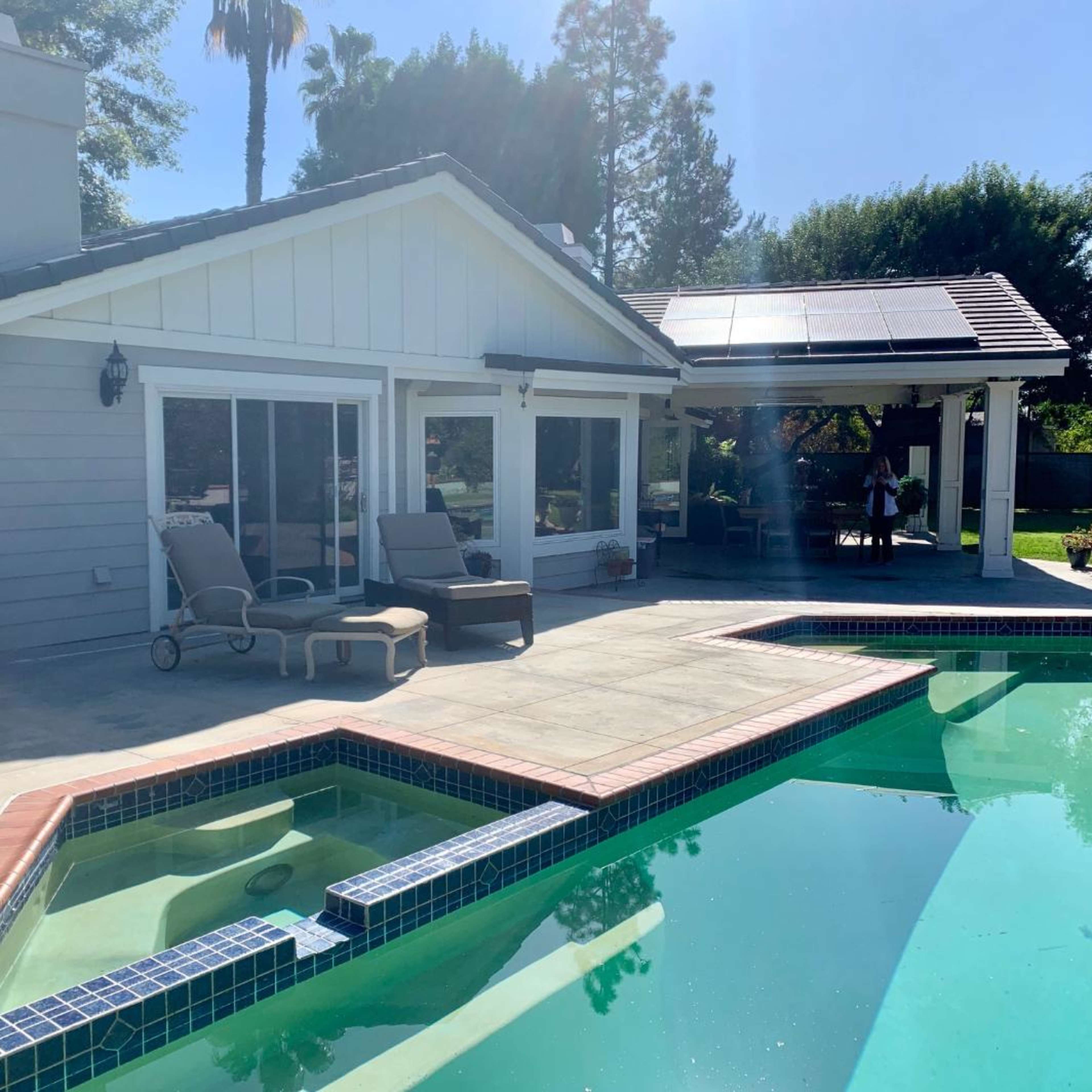 A backyard with a swimming pool, lounge chairs, and a house featuring solar panels and large windows.