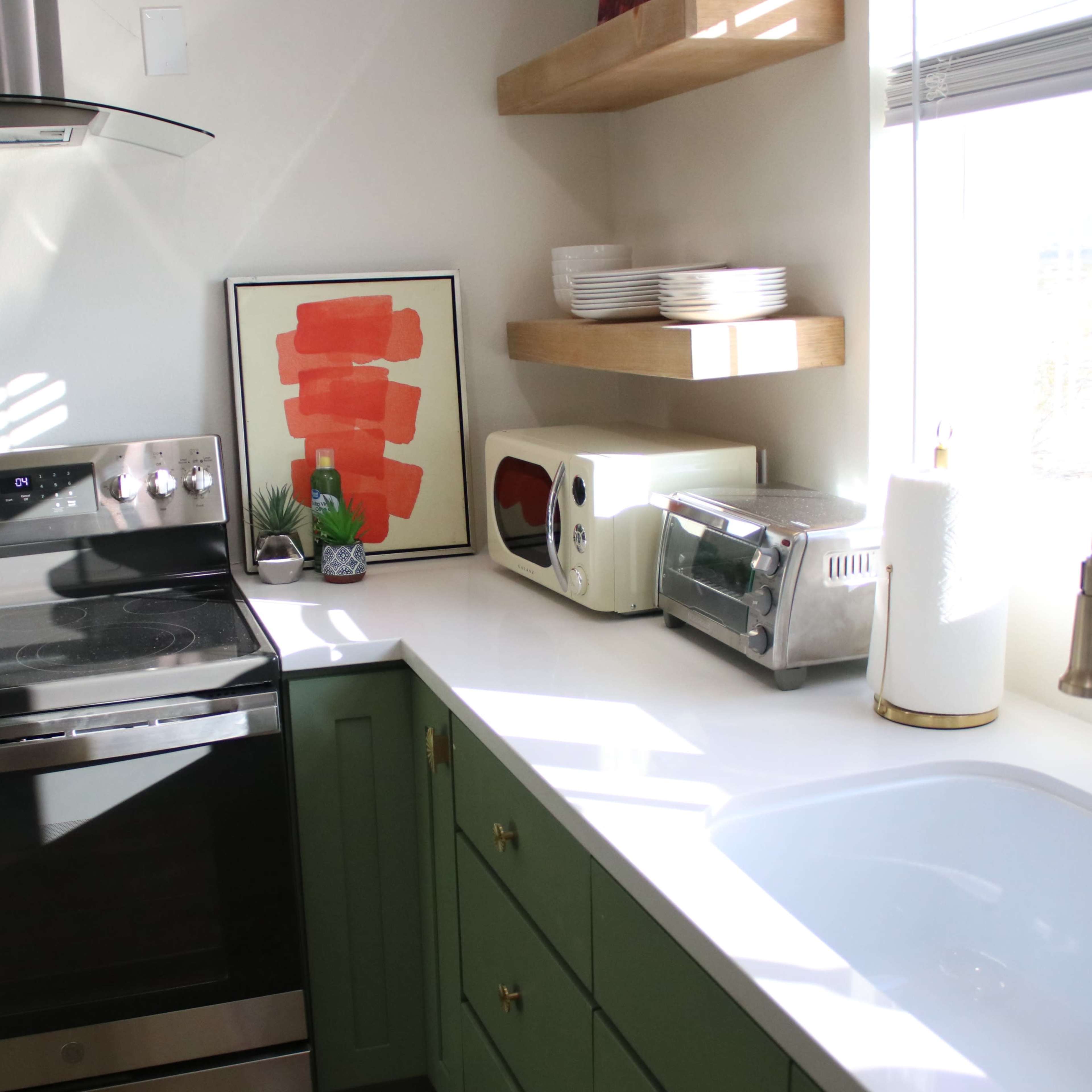 A modern kitchen features a stove, sink, and various appliances, with open shelves displaying plates and a framed artwork.