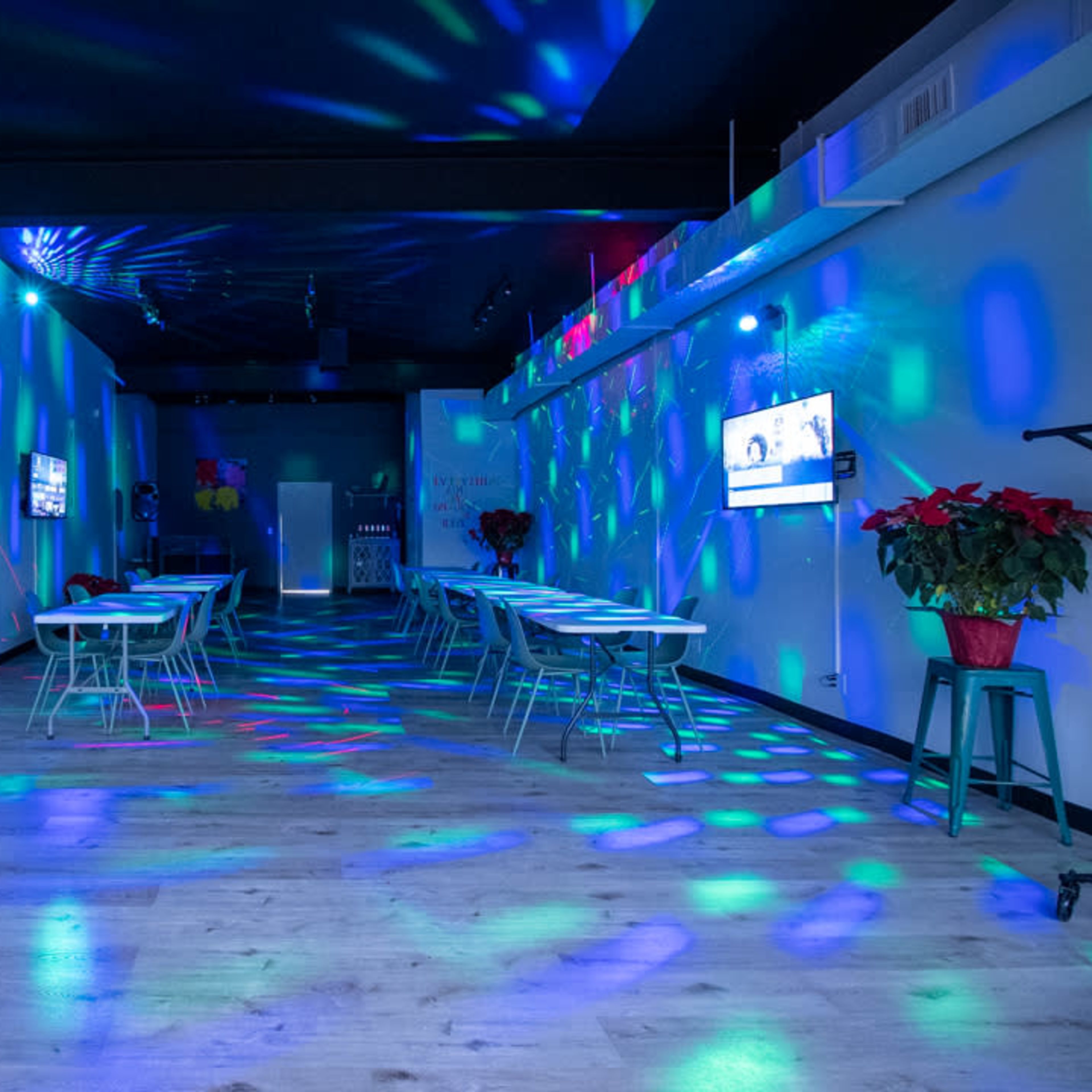 A party venue is illuminated with multicolored lights, featuring decorated tables and a large mirror with a birthday message.