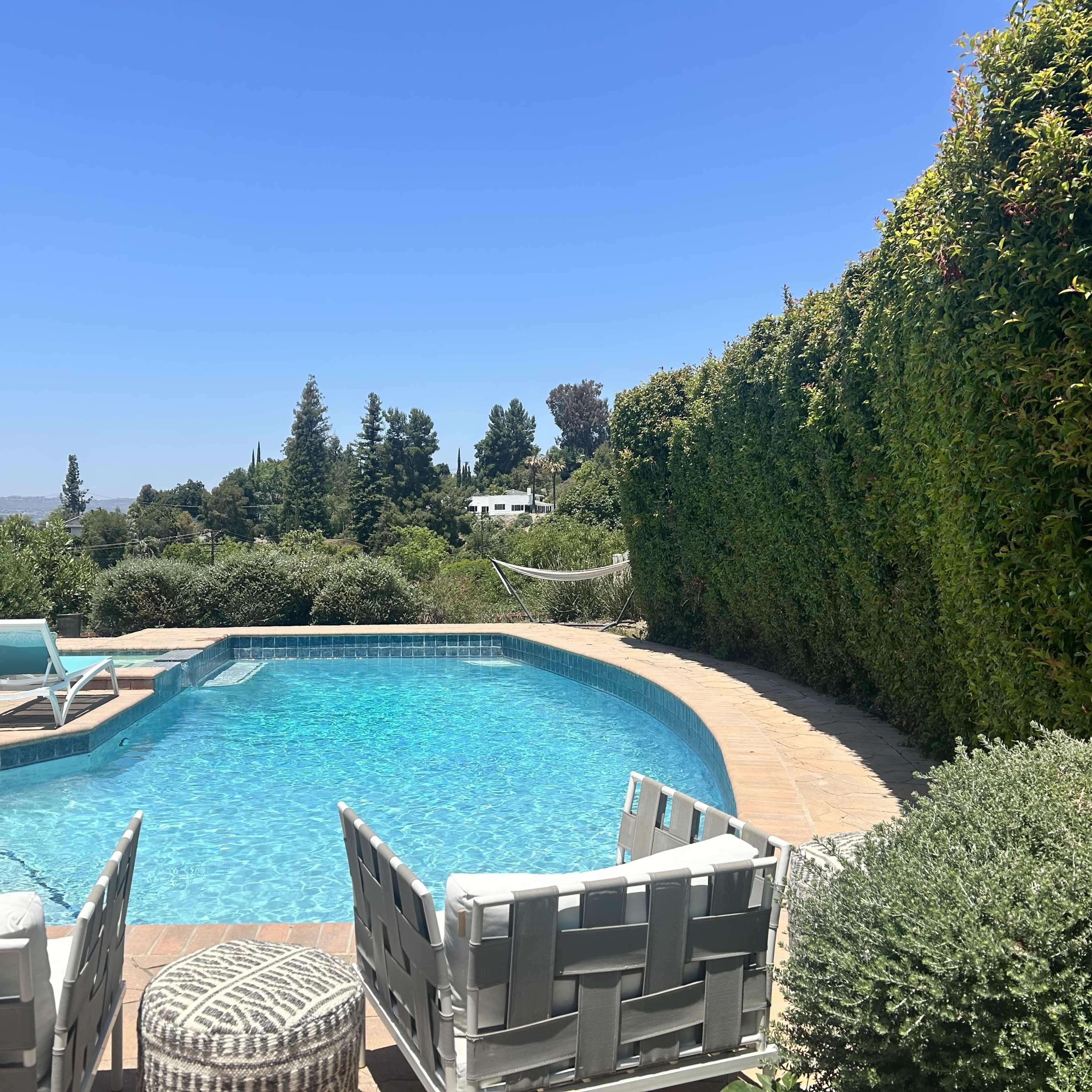 A swimming pool surrounded by lounge chairs and greenery under a clear blue sky.