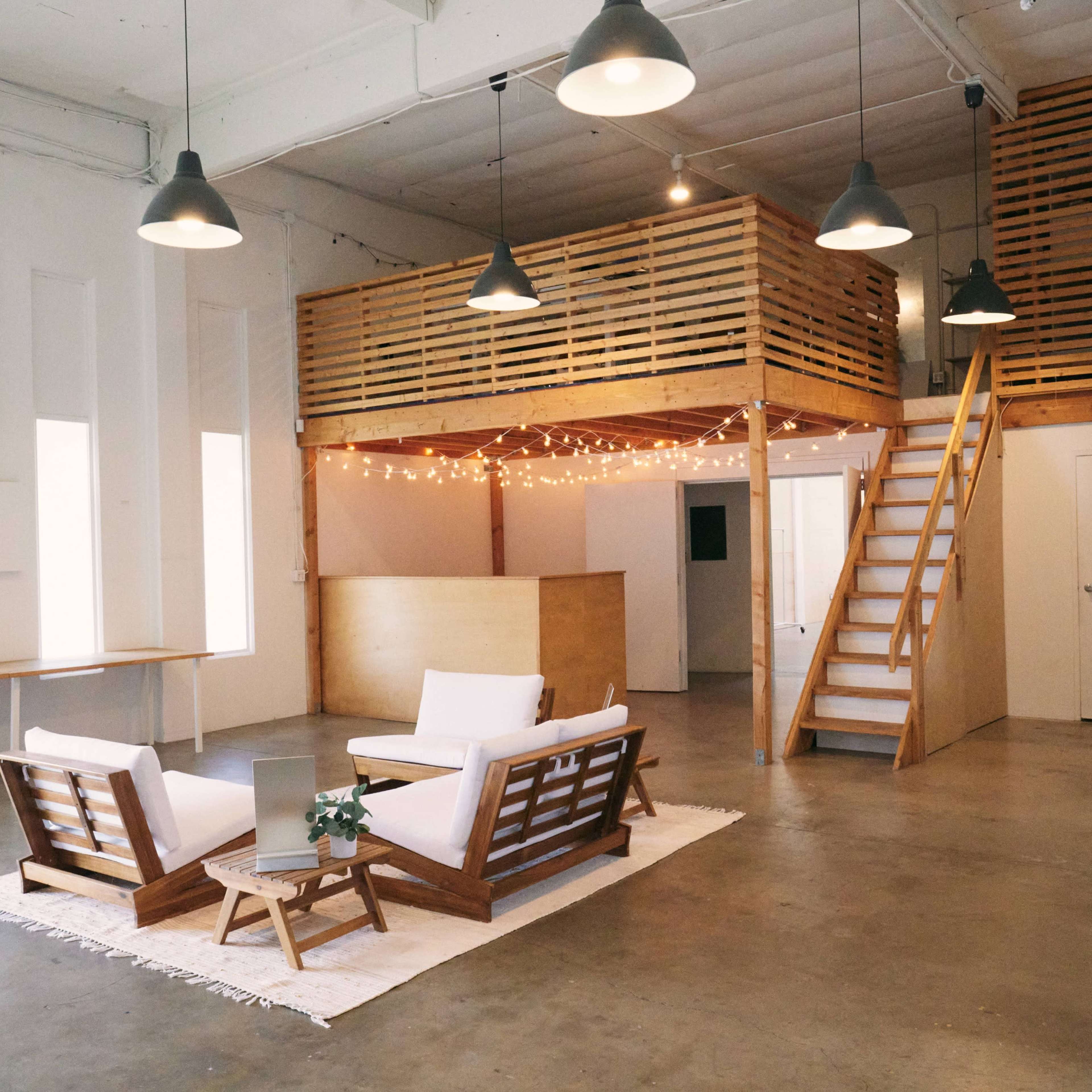A spacious, modern interior with a seating area featuring two white chairs, a wooden counter, and a lofted space accessed by stairs.