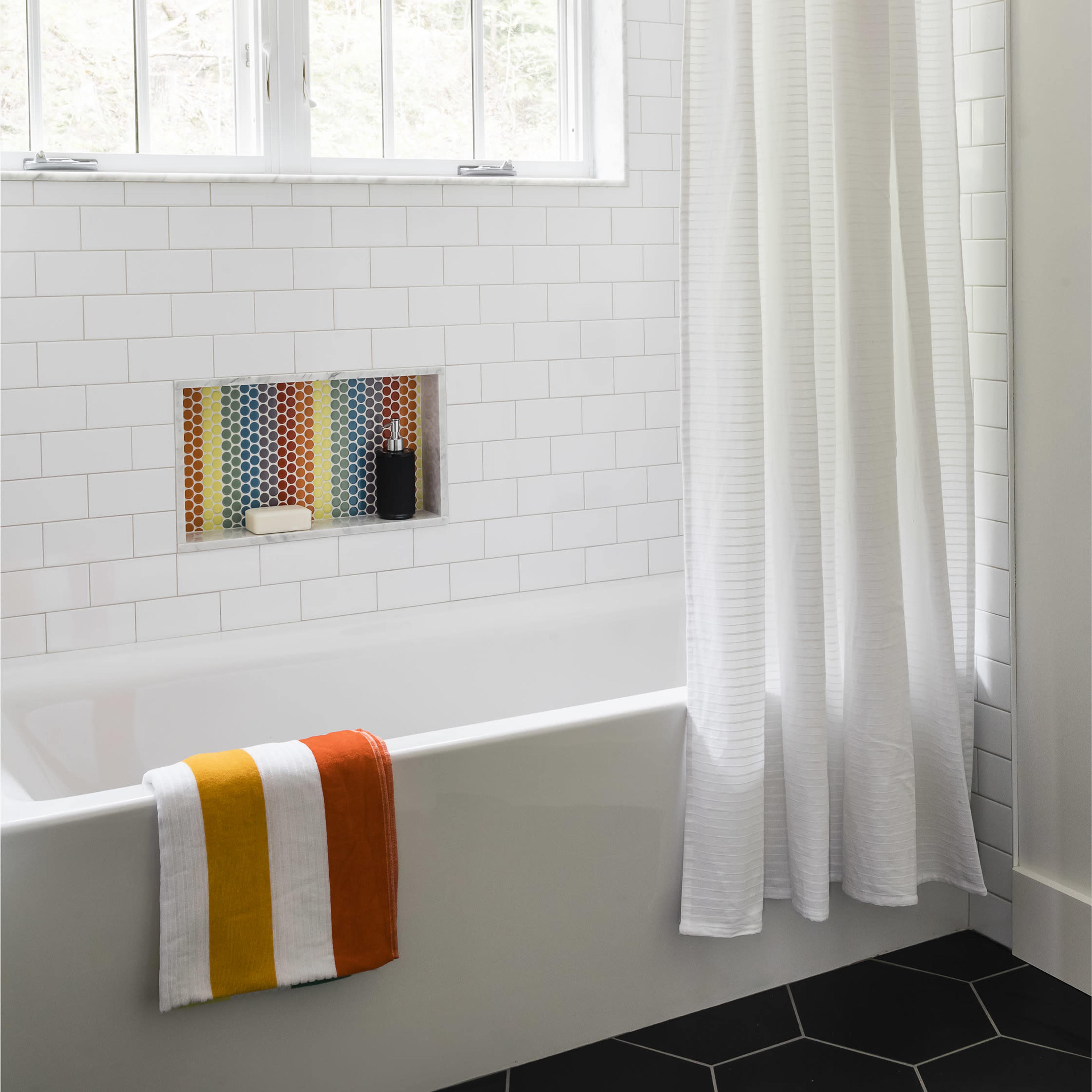 A bathroom featuring a white bathtub with a shower curtain, a tiled wall, and a colorful tile niche containing toiletries.