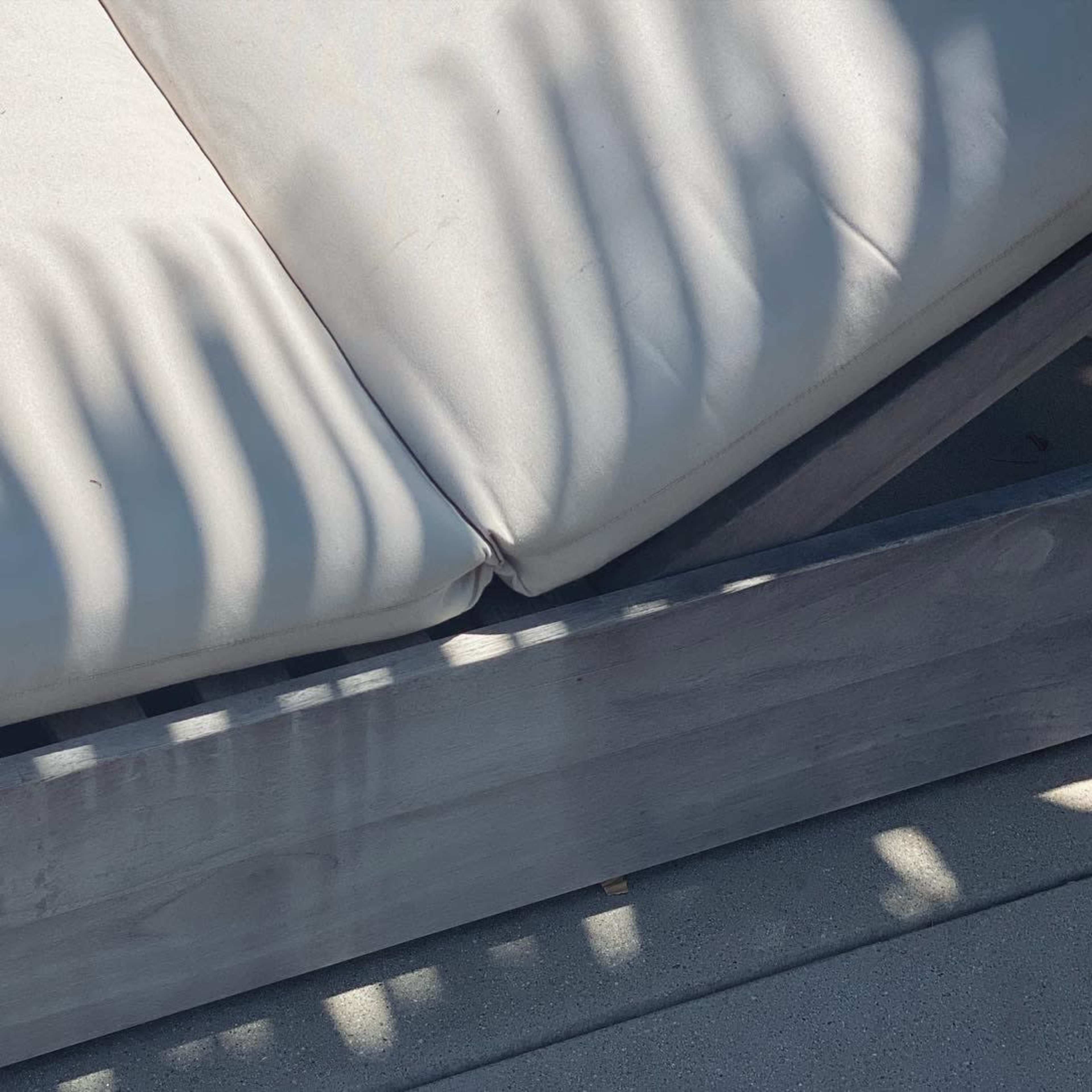 The corner of a cushioned lounge chair with light and shadow patterns created by the surrounding environment.