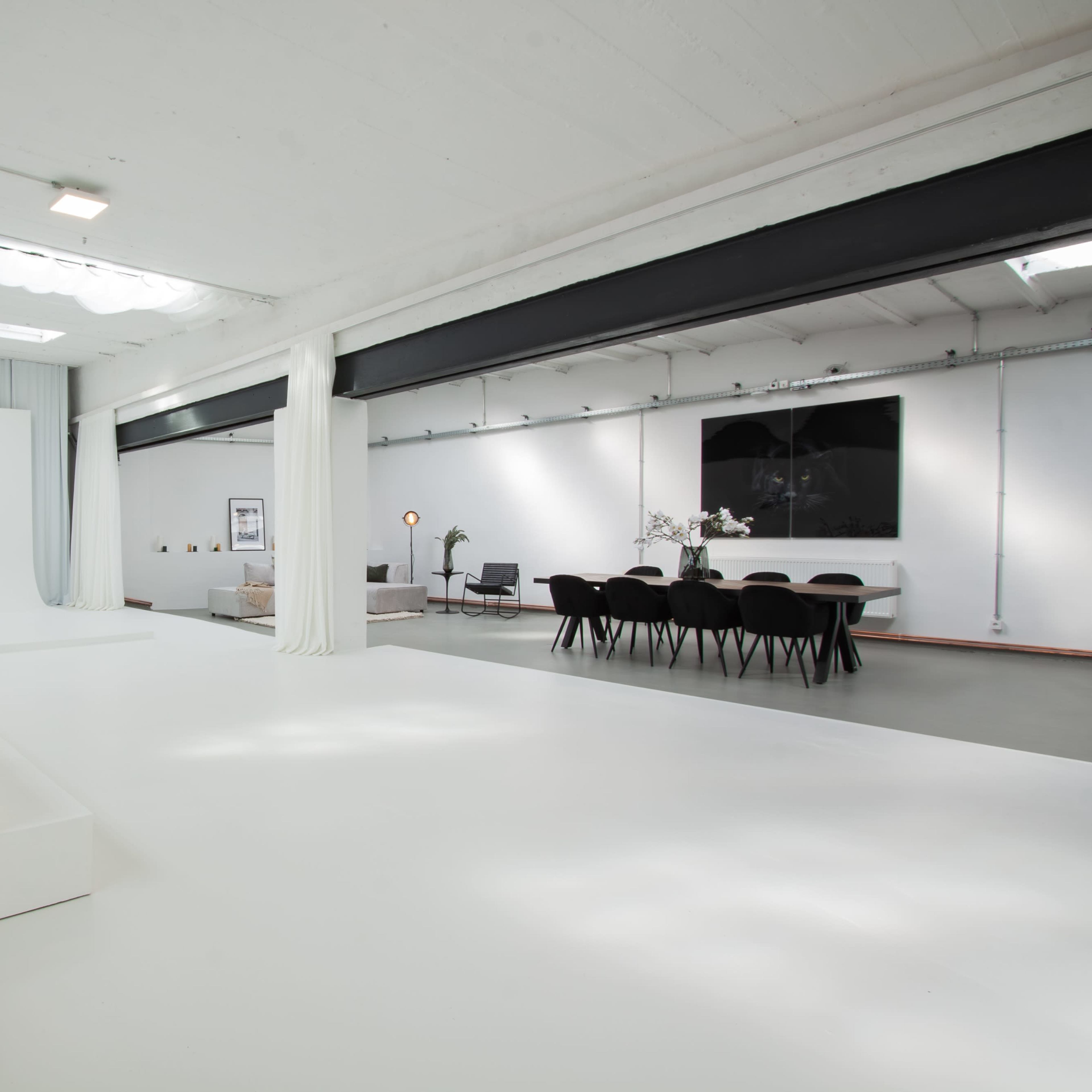 A spacious, modern interior with a white floor, a blank backdrop, and a dining area featuring a table and chairs.
