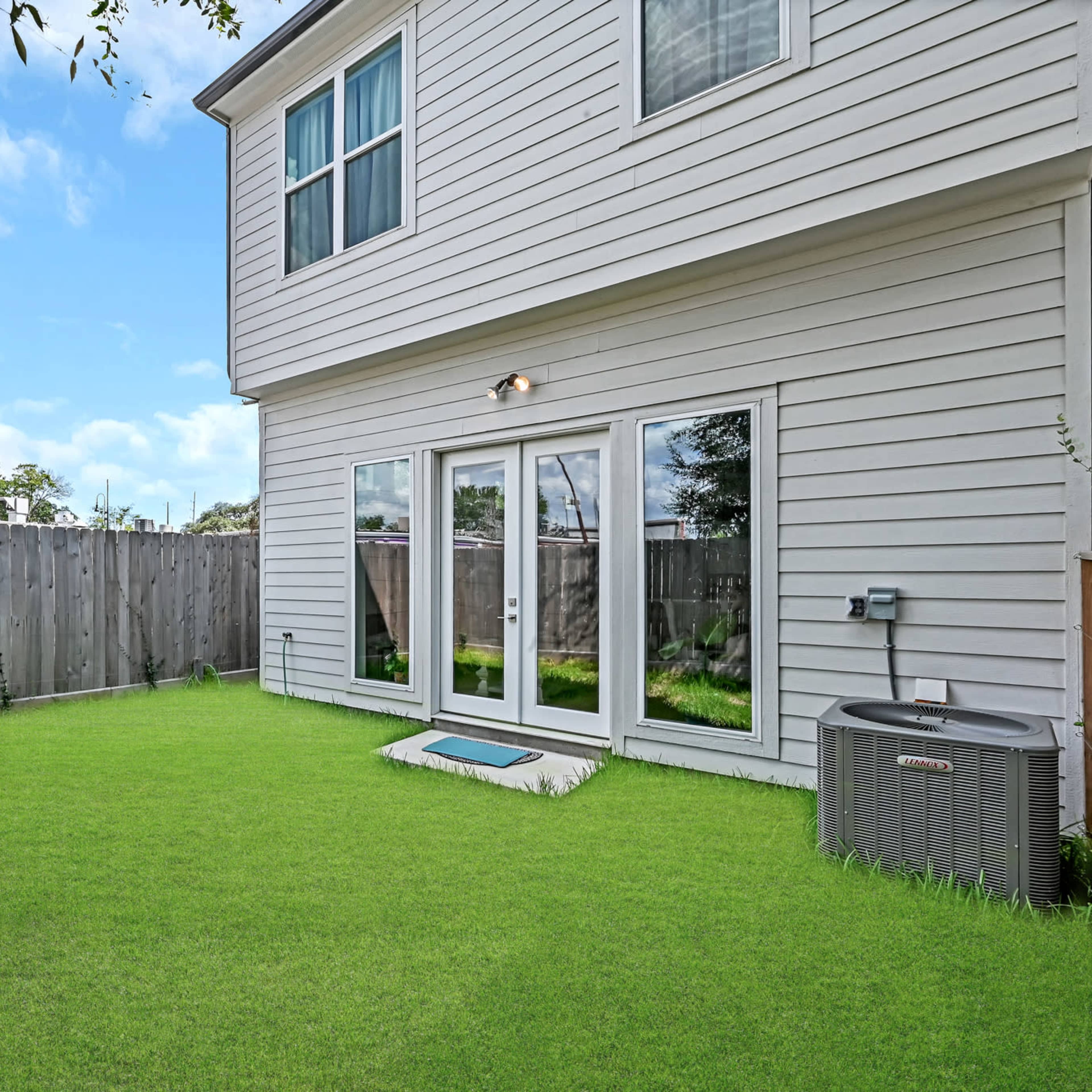 A backyard with a well-manicured green lawn, a wooden fence, and a two-story home with sliding glass doors.