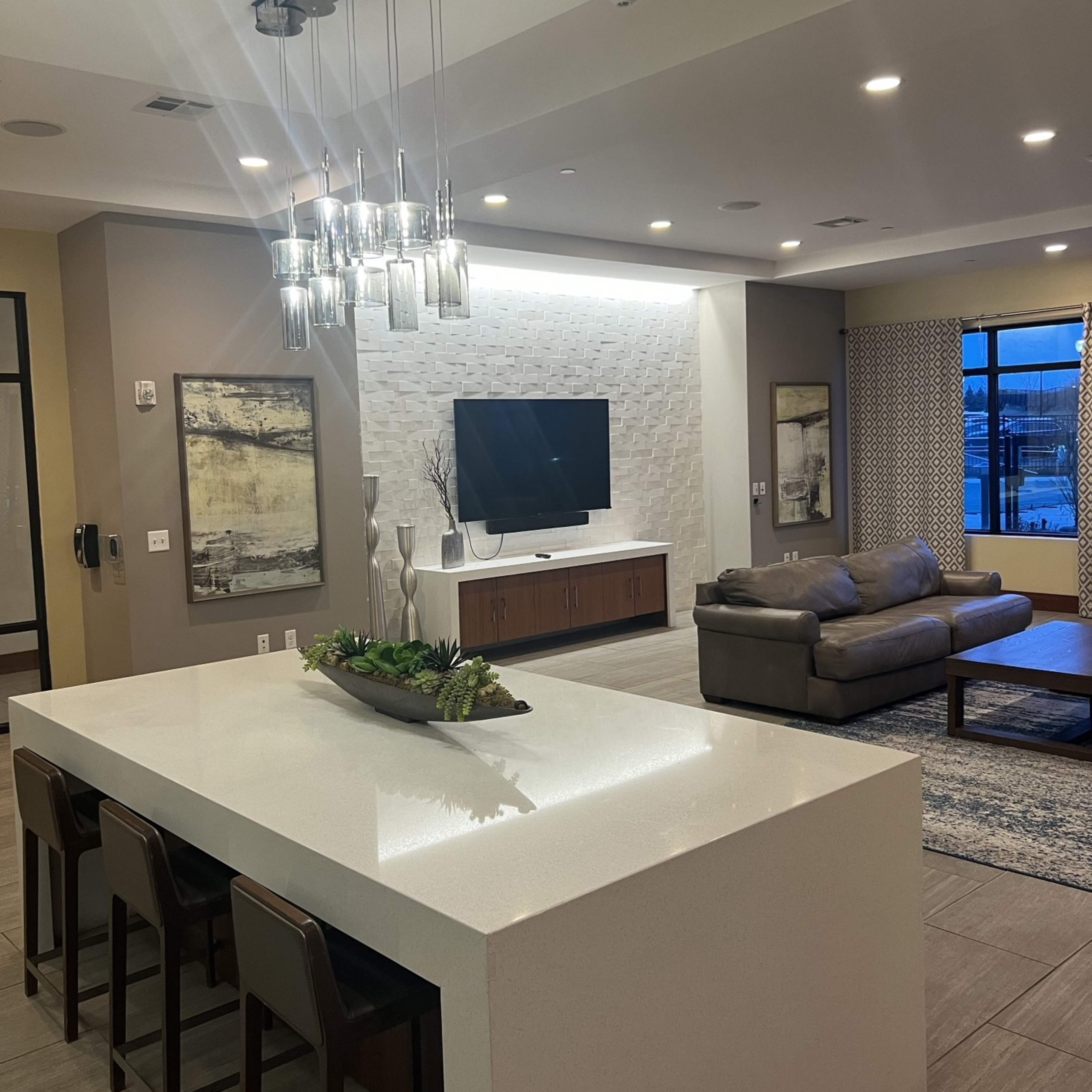 A modern living space with a white countertop island, a television mounted on the wall, and a gray sofa set in a well-lit room.