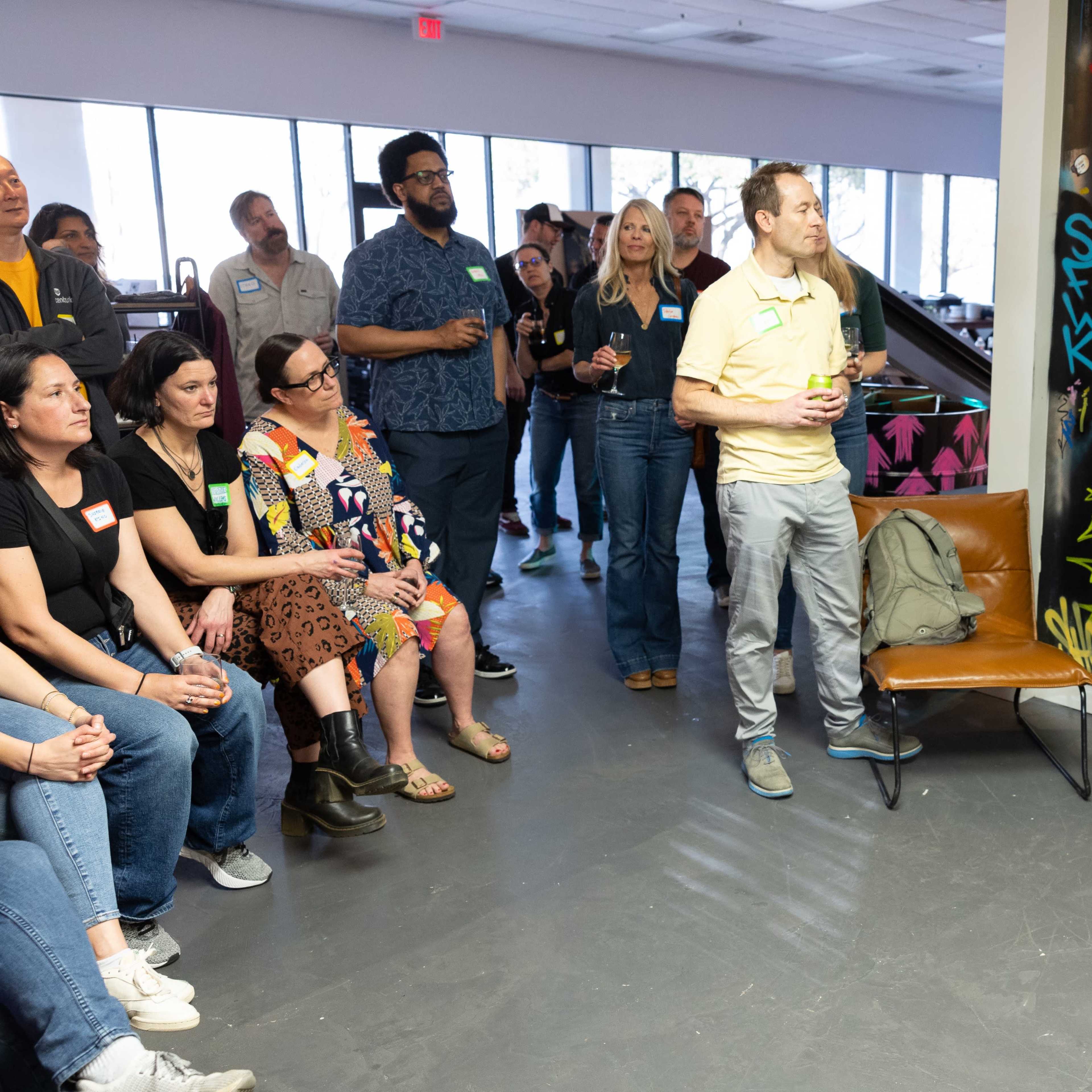 A group of people listens attentively to a speaker in a room with colorful graffiti on the walls.