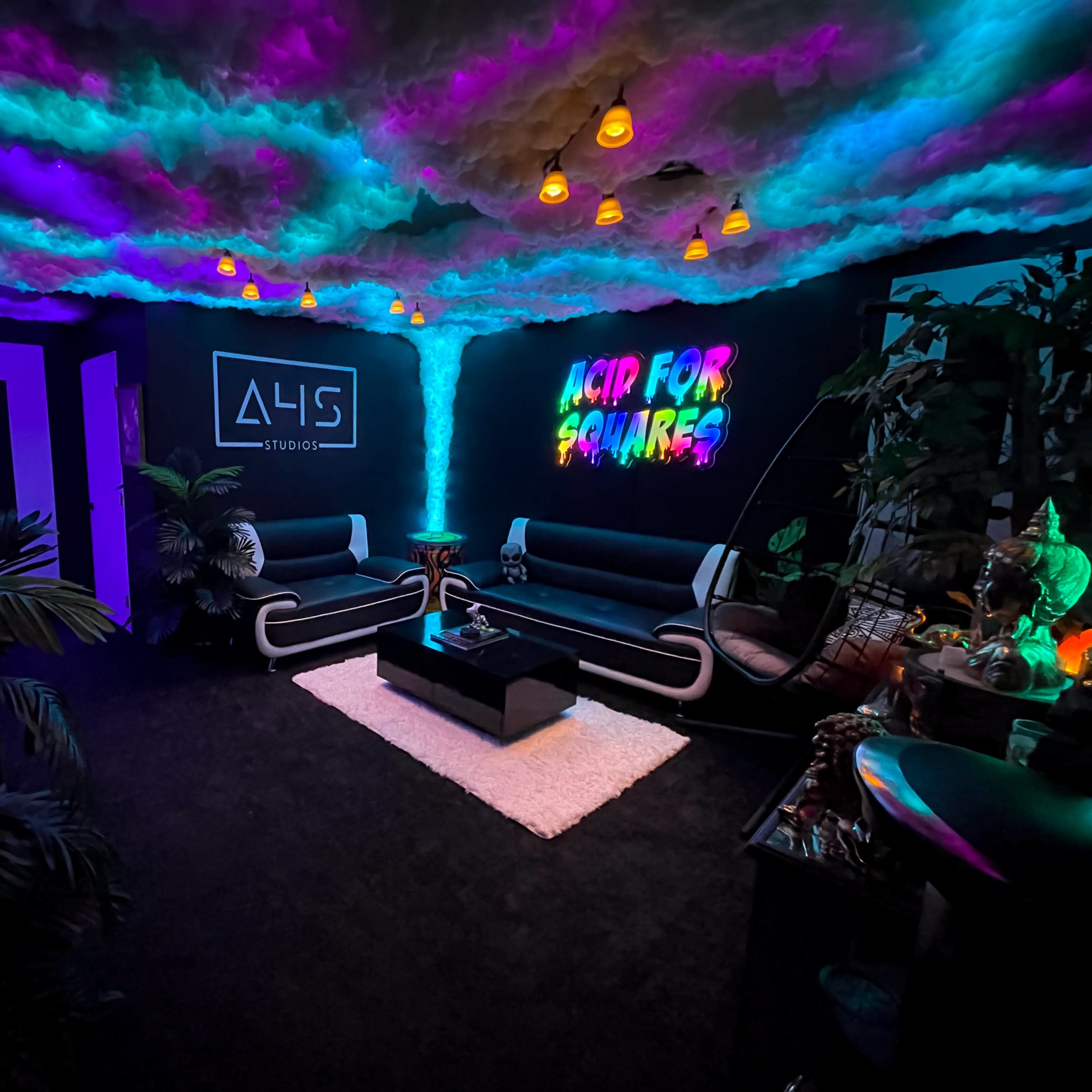A vibrant lounge area featuring neon colors on the ceiling, modern furniture, and a wall display with the text "ACID FOR SQUARES."