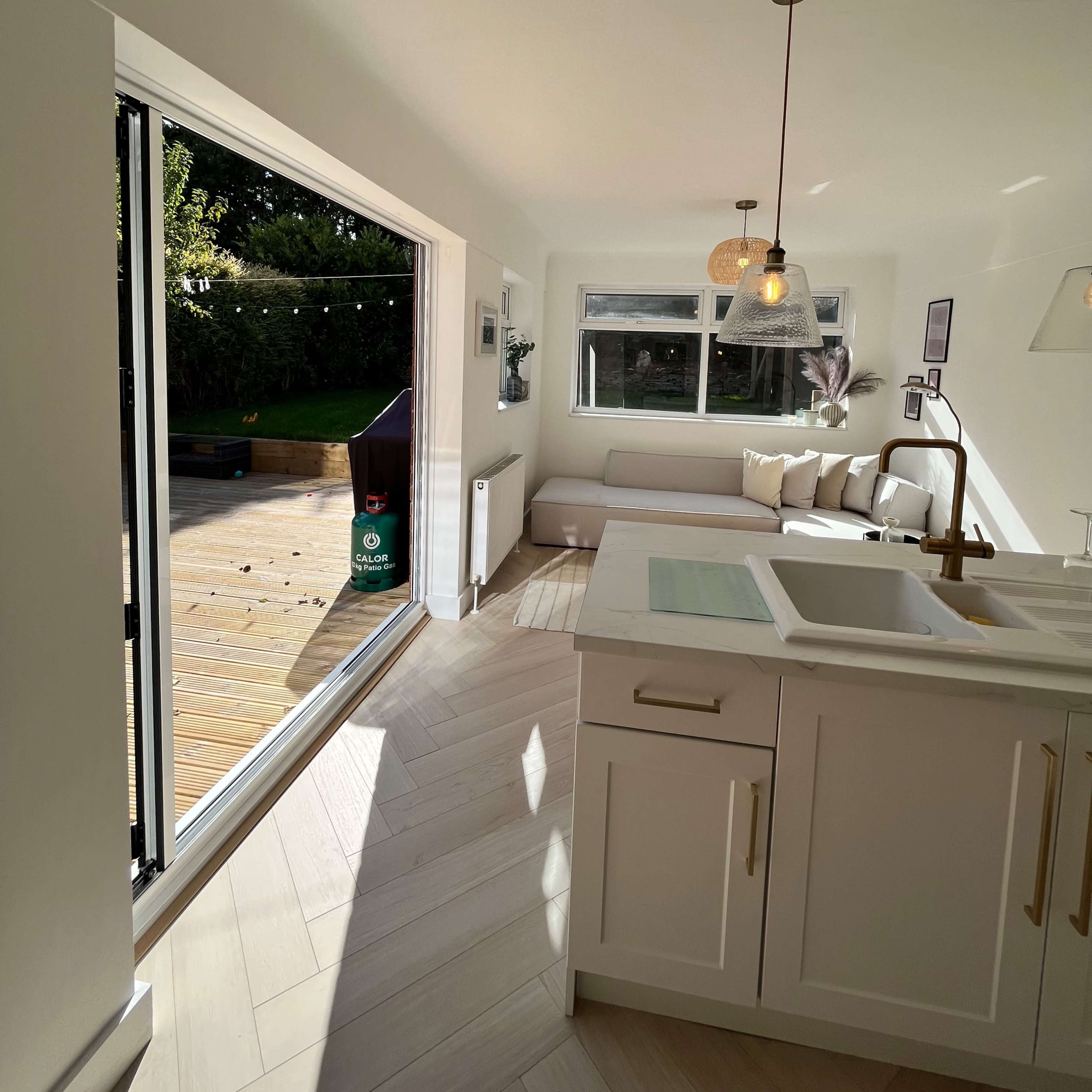 A bright kitchen opens to a deck through a sliding glass door, featuring modern cabinetry and a window seat.