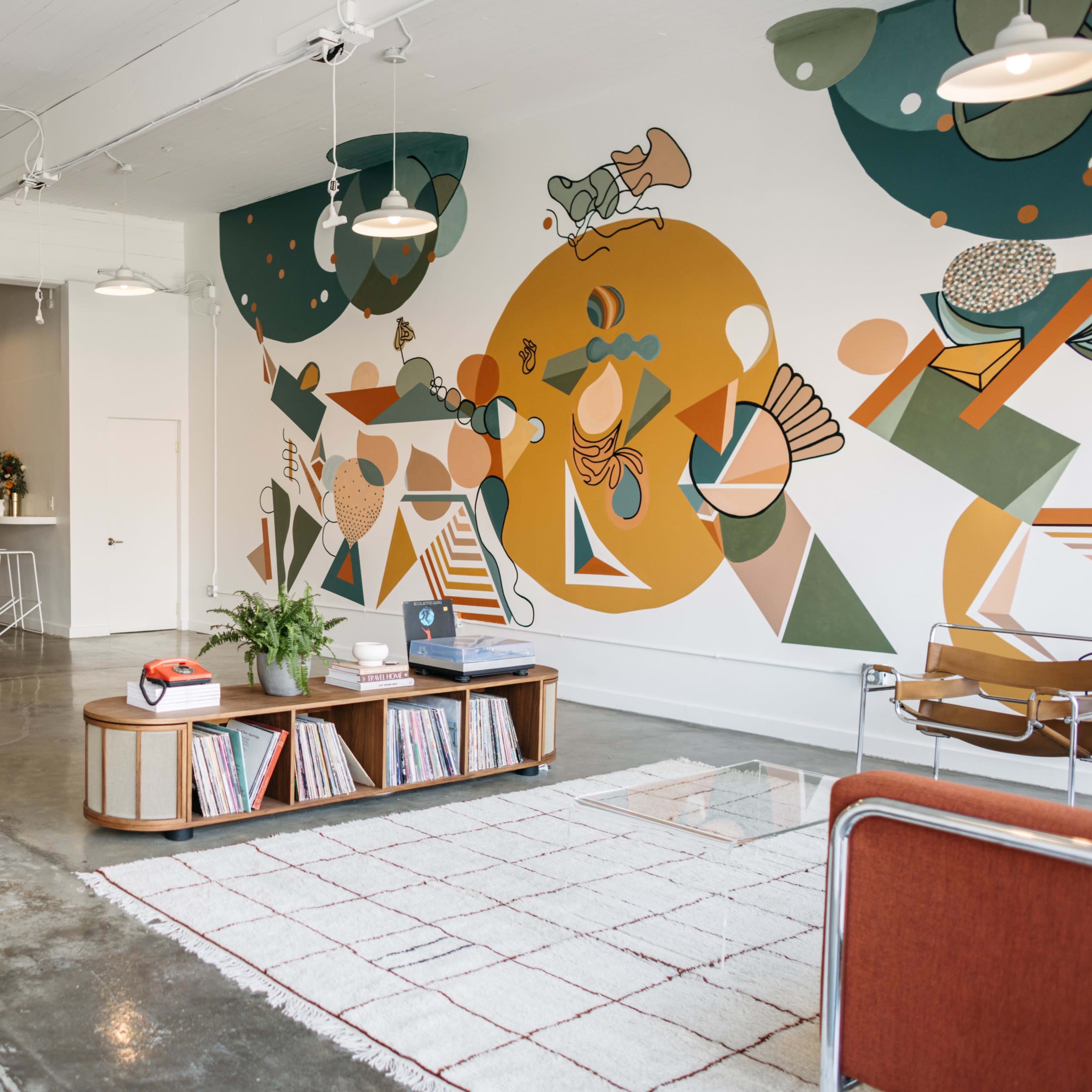 The scene features a modern, open-concept living space with a mural on one wall, a coffee table displaying records, and a cozy seating area.