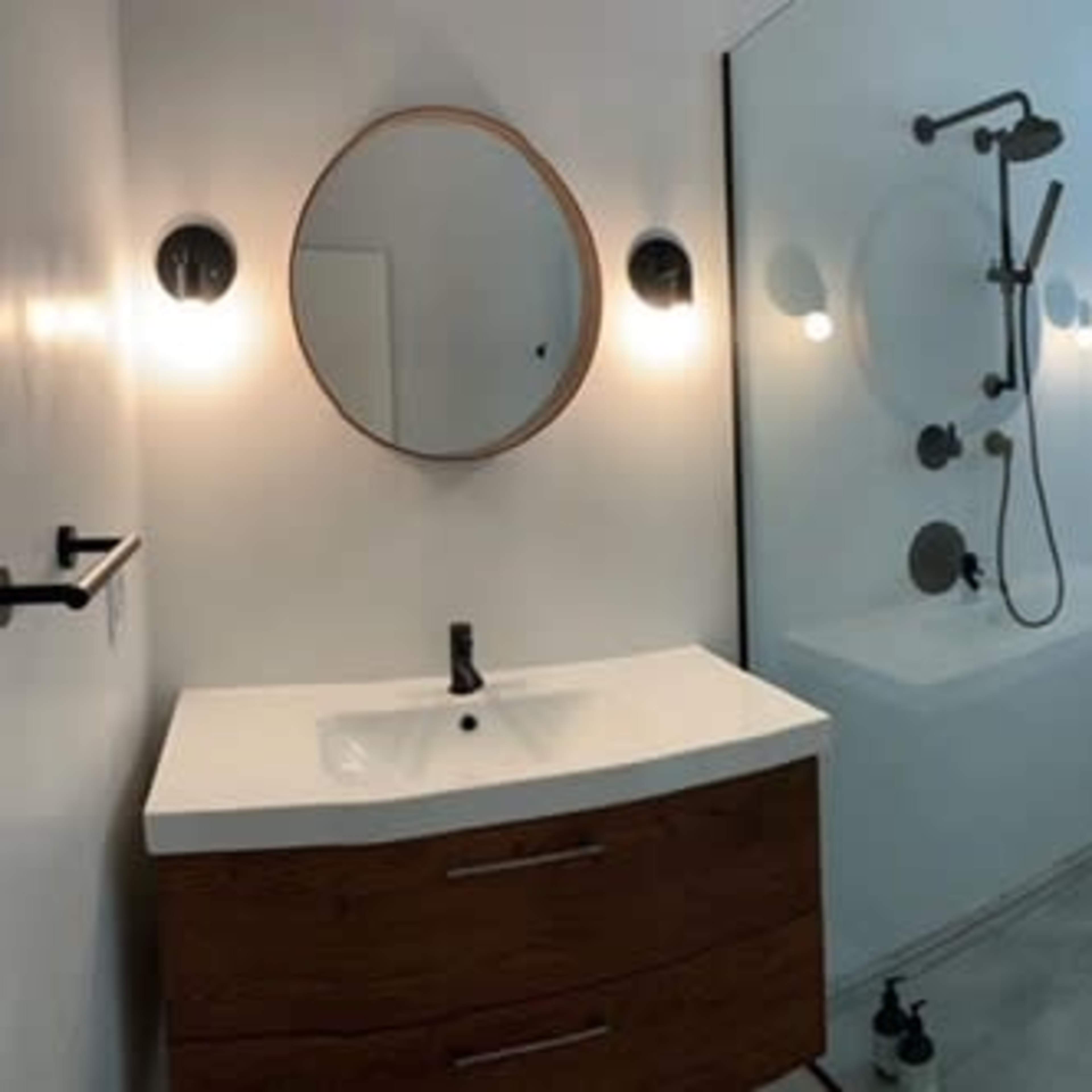 A modern bathroom featuring a freestanding bathtub, a glass shower enclosure, a wall-mounted sink with a wooden vanity, and a round mirror.