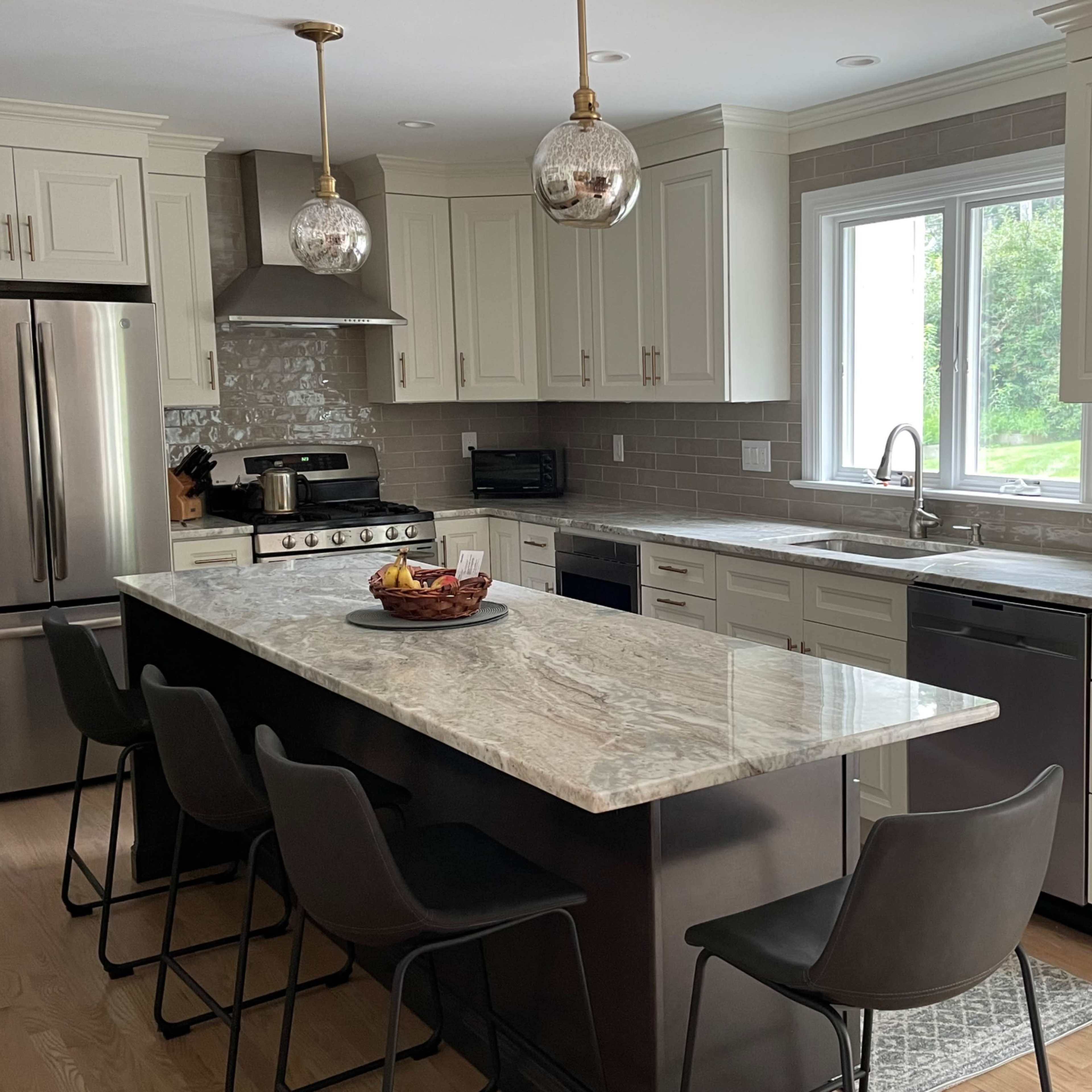 A modern kitchen with white cabinetry, stainless steel appliances, a large marble island, and bar seating.