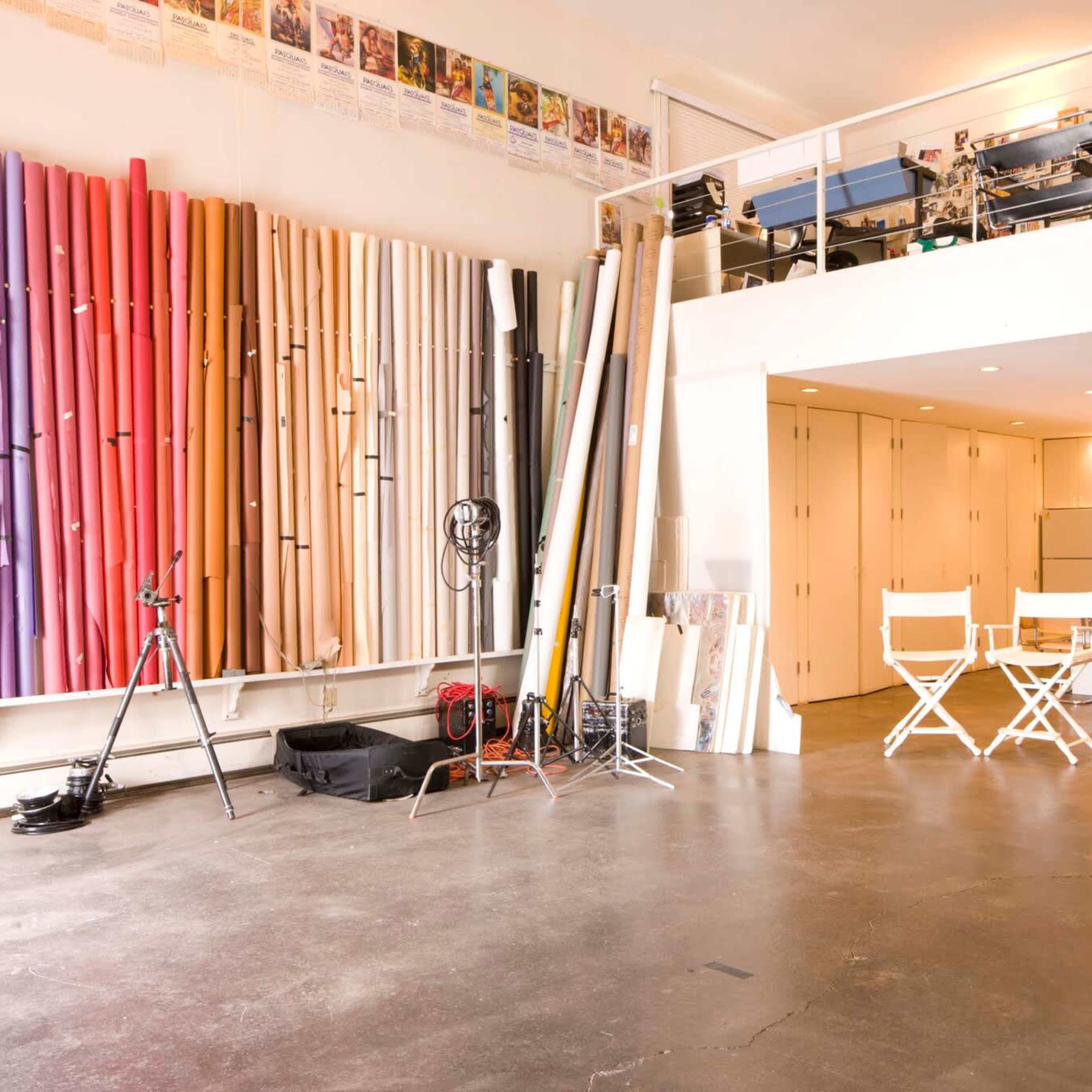 A spacious studio with a variety of colored backdrops against one wall and a kitchen area along with a dining table and chairs in the center.