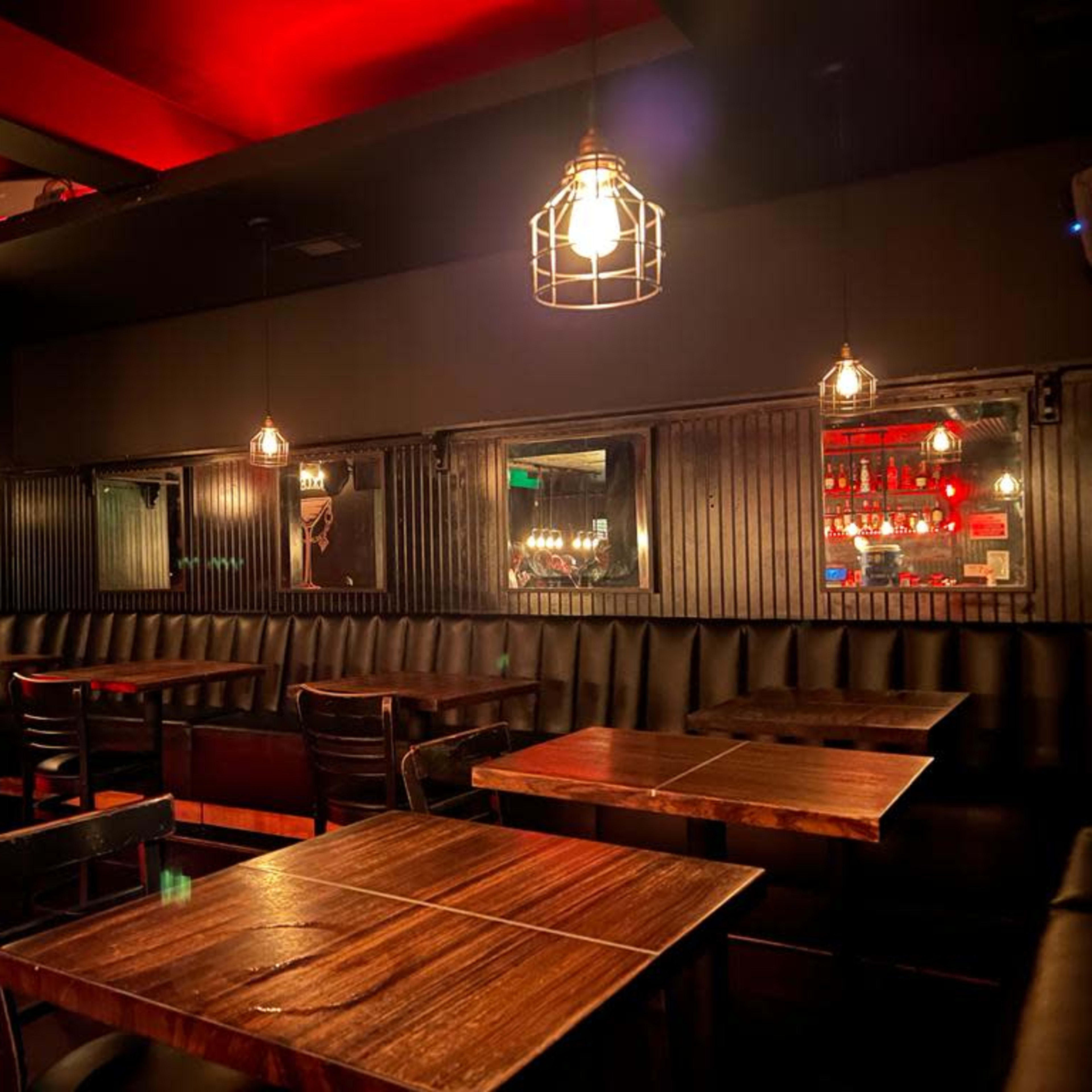 A dimly lit restaurant interior with wooden tables, black leather seating, and illuminated pendant lights hanging from the ceiling.