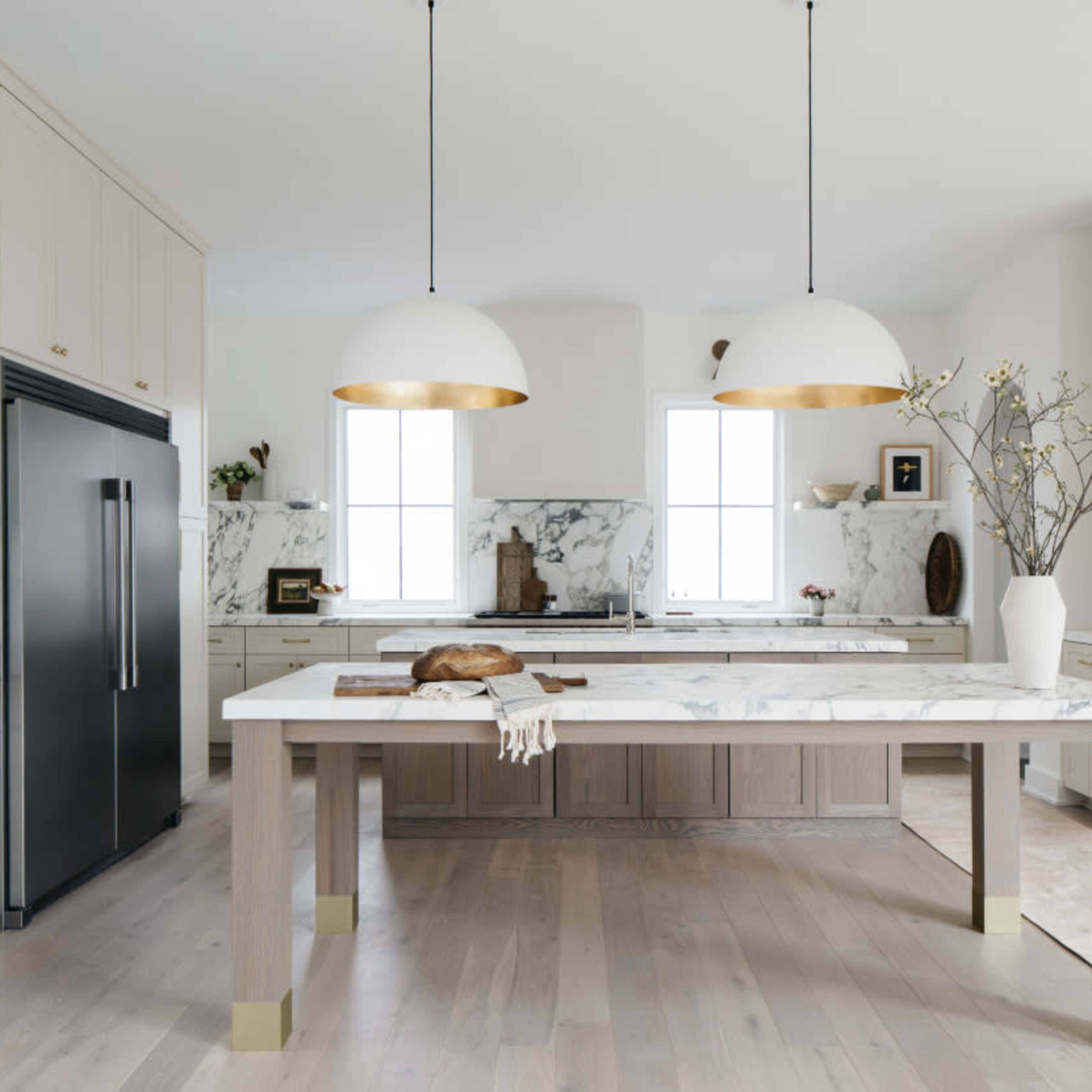 A modern kitchen features a marble-topped island with two large pendant lights, sleek cabinetry, and a dark refrigerator.