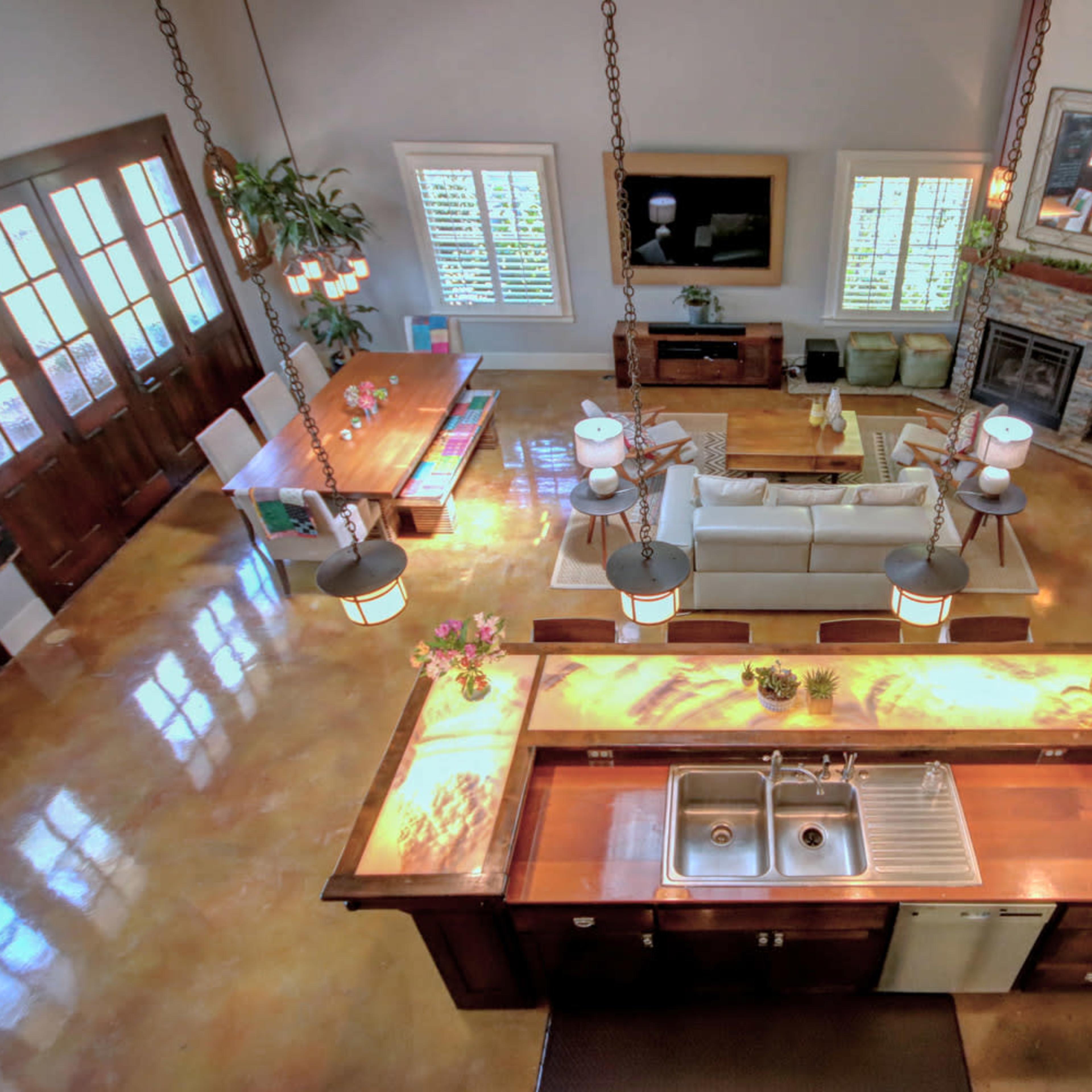 A spacious open-concept living area and kitchen with a central island, large windows, and wooden furnishings.