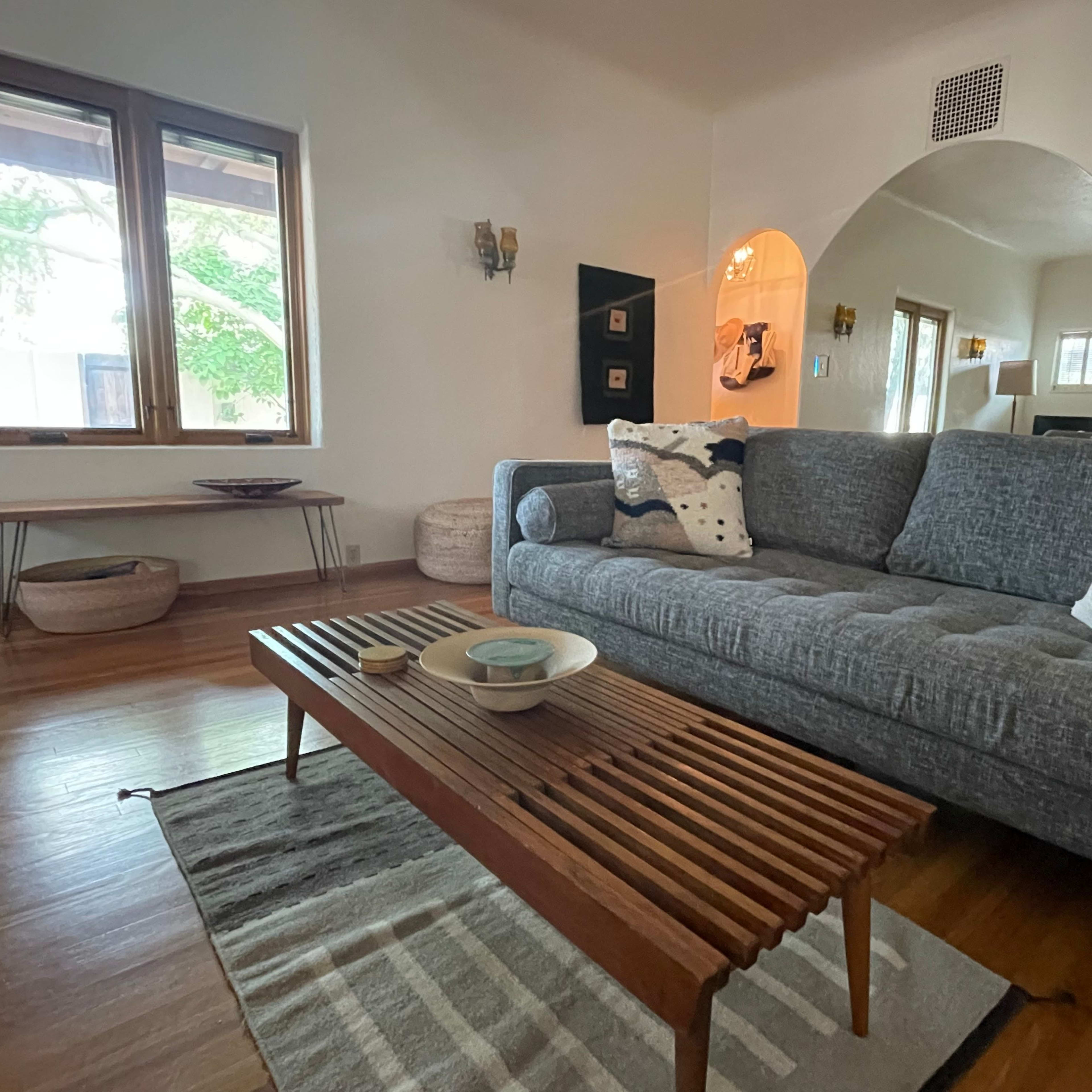 A living room featuring a gray couch, a wooden coffee table, and large windows allowing natural light in.