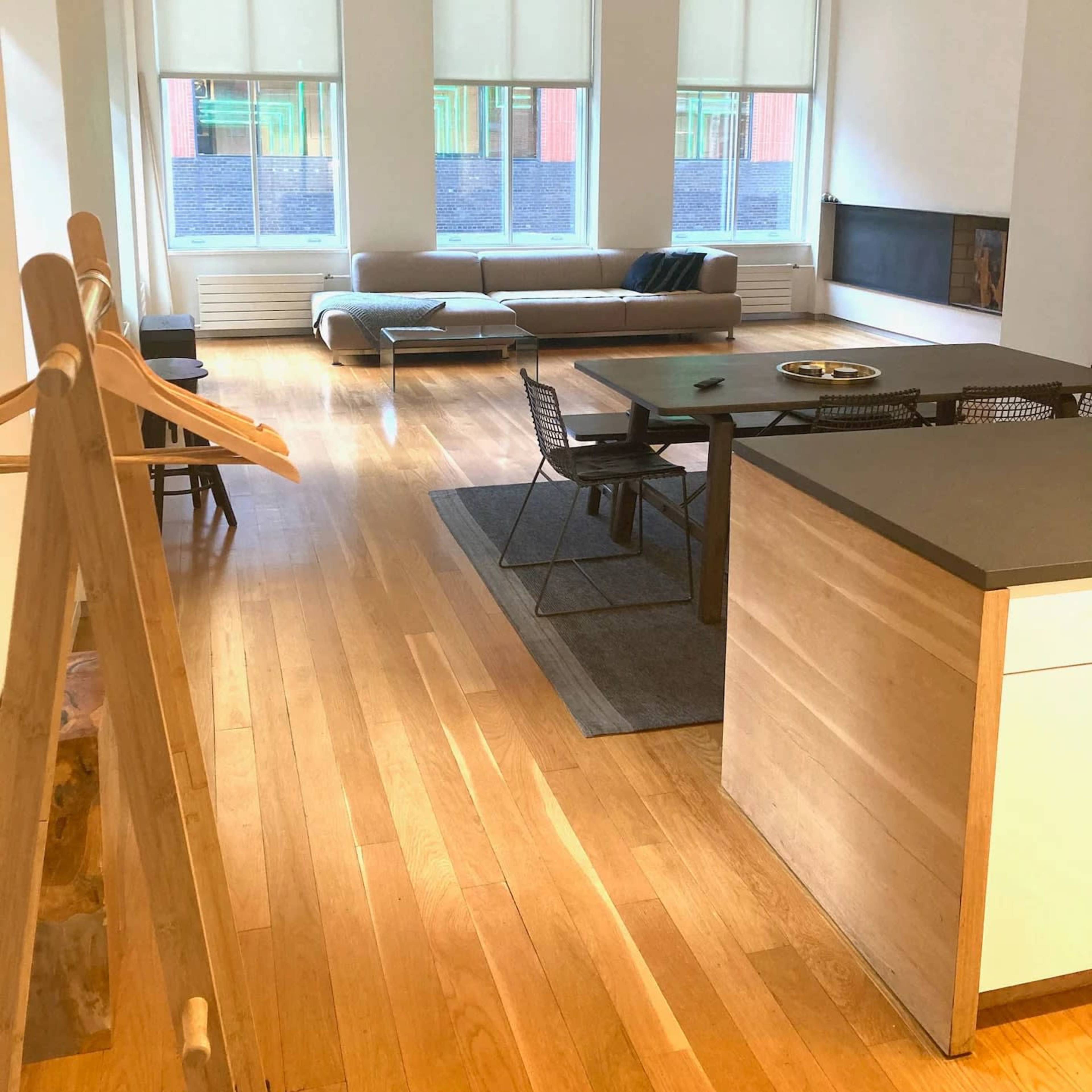 A modern open-concept living space features a dining area, a kitchen island, and a seating area with large windows allowing natural light to enter.