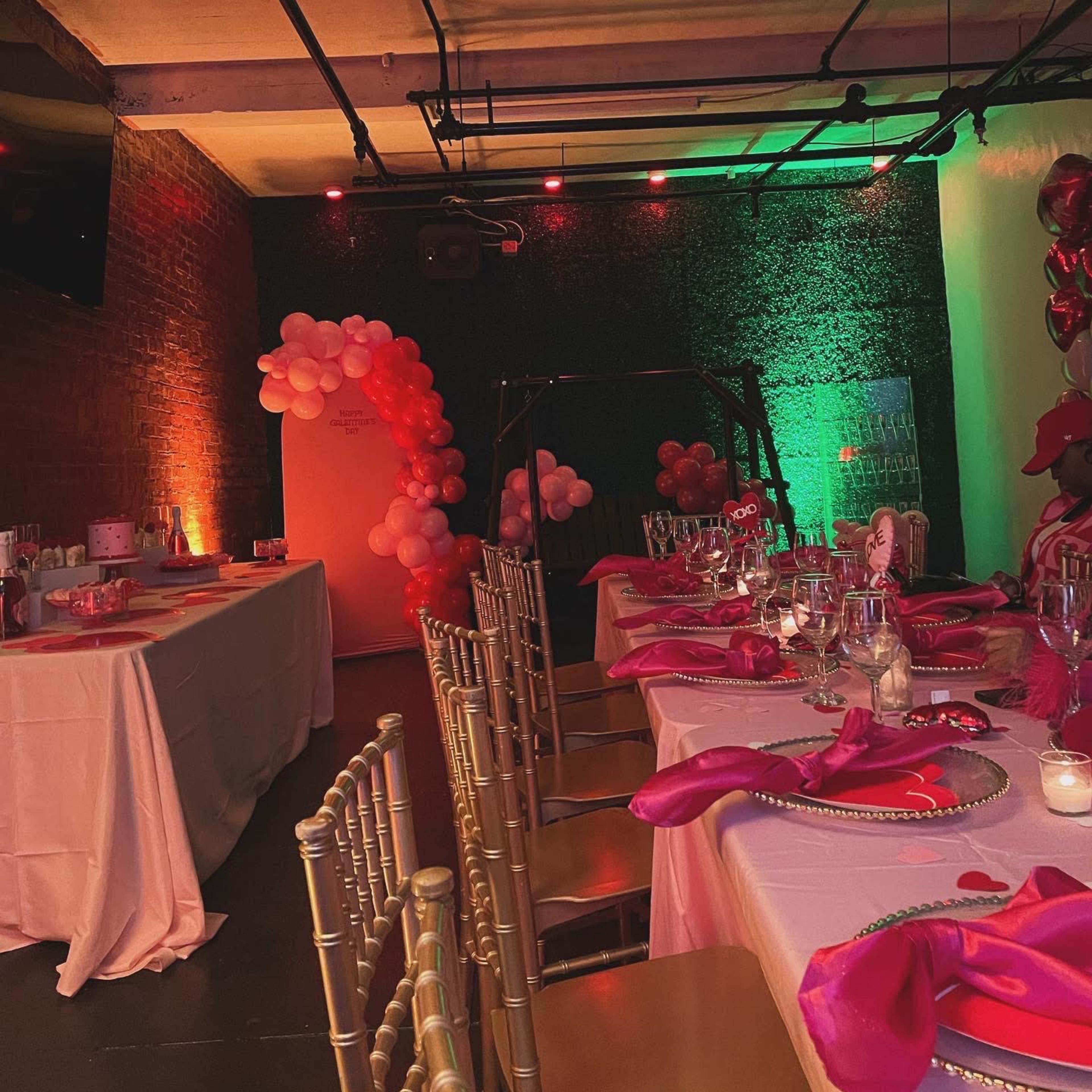 A decorated event space with gold chairs, pink table settings, and a backdrop of balloons.