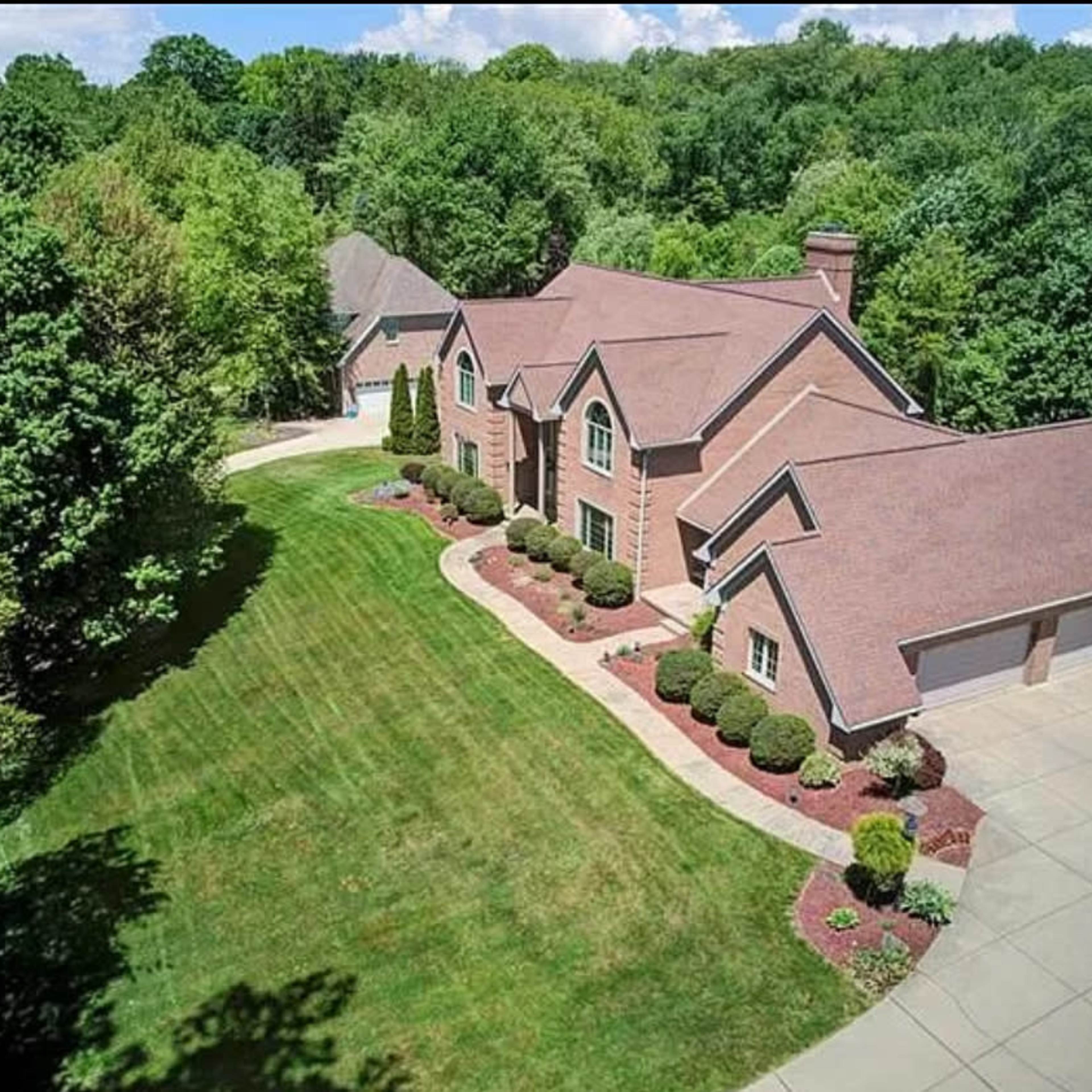 A large, two-story brick house with a sloped roof, surrounded by manicured lawns and trees.