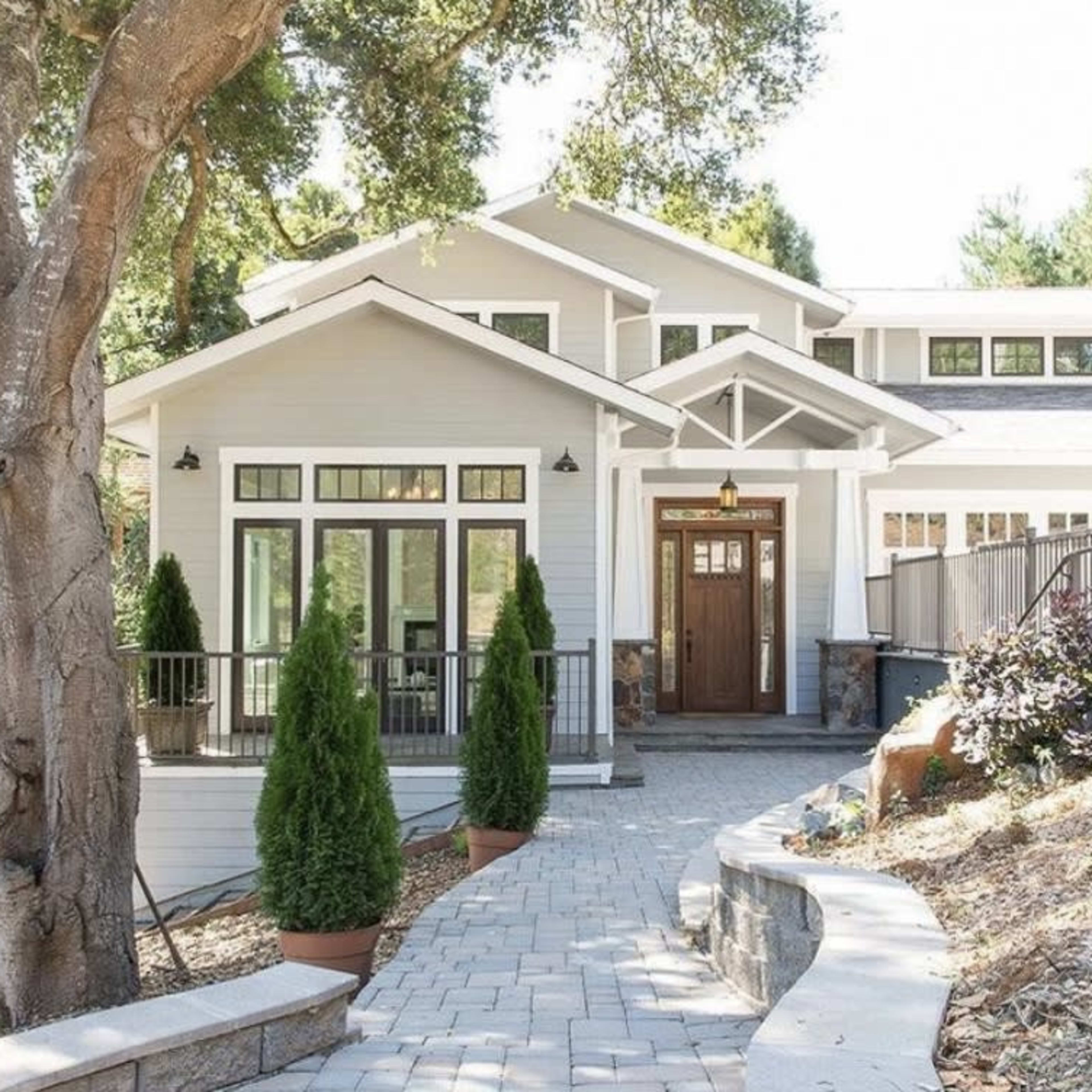 A modern two-story house with a wooden front door is surrounded by greenery and features landscaped pathways and planters.