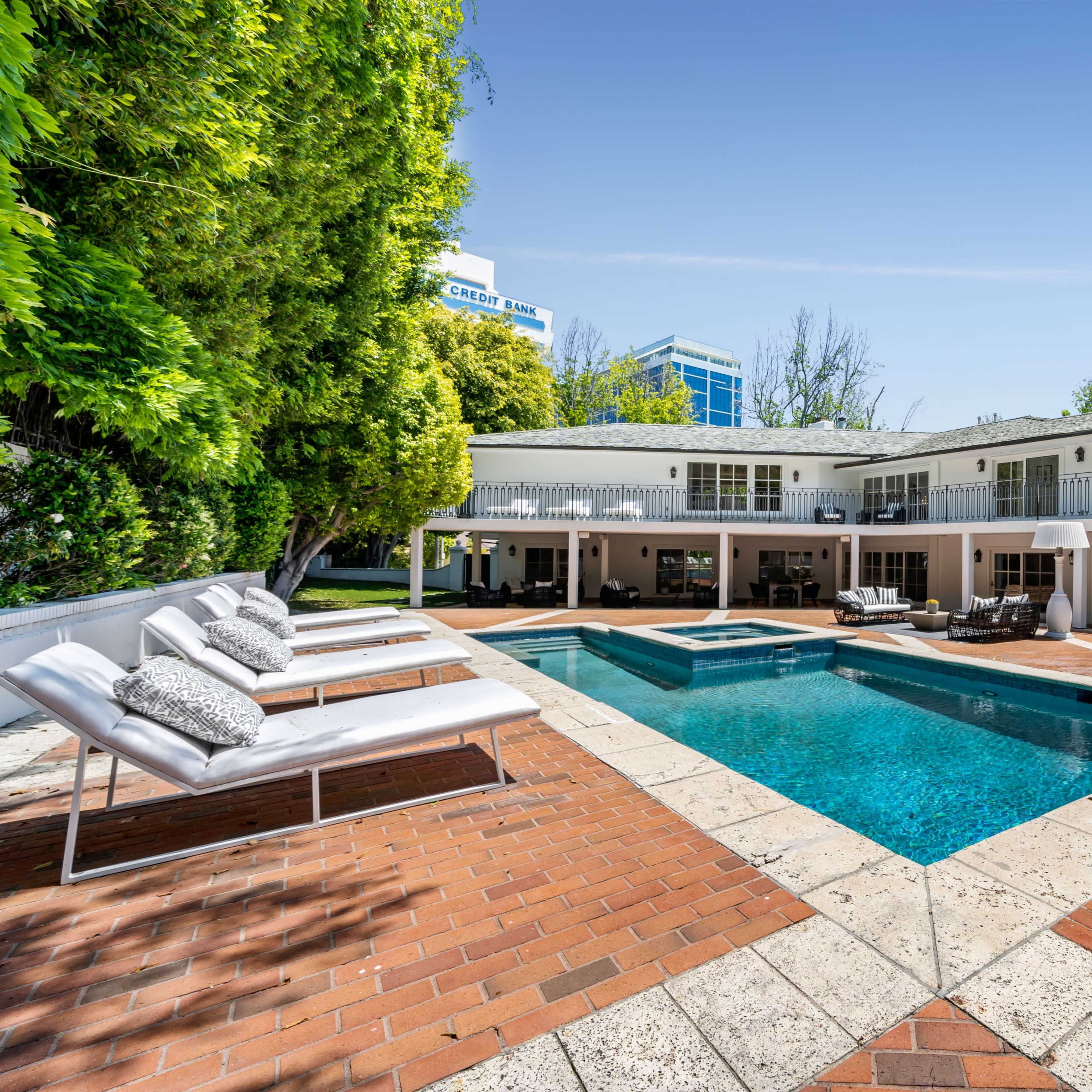 A modern two-story house with a swimming pool and lounge chairs set in a landscaped outdoor area.