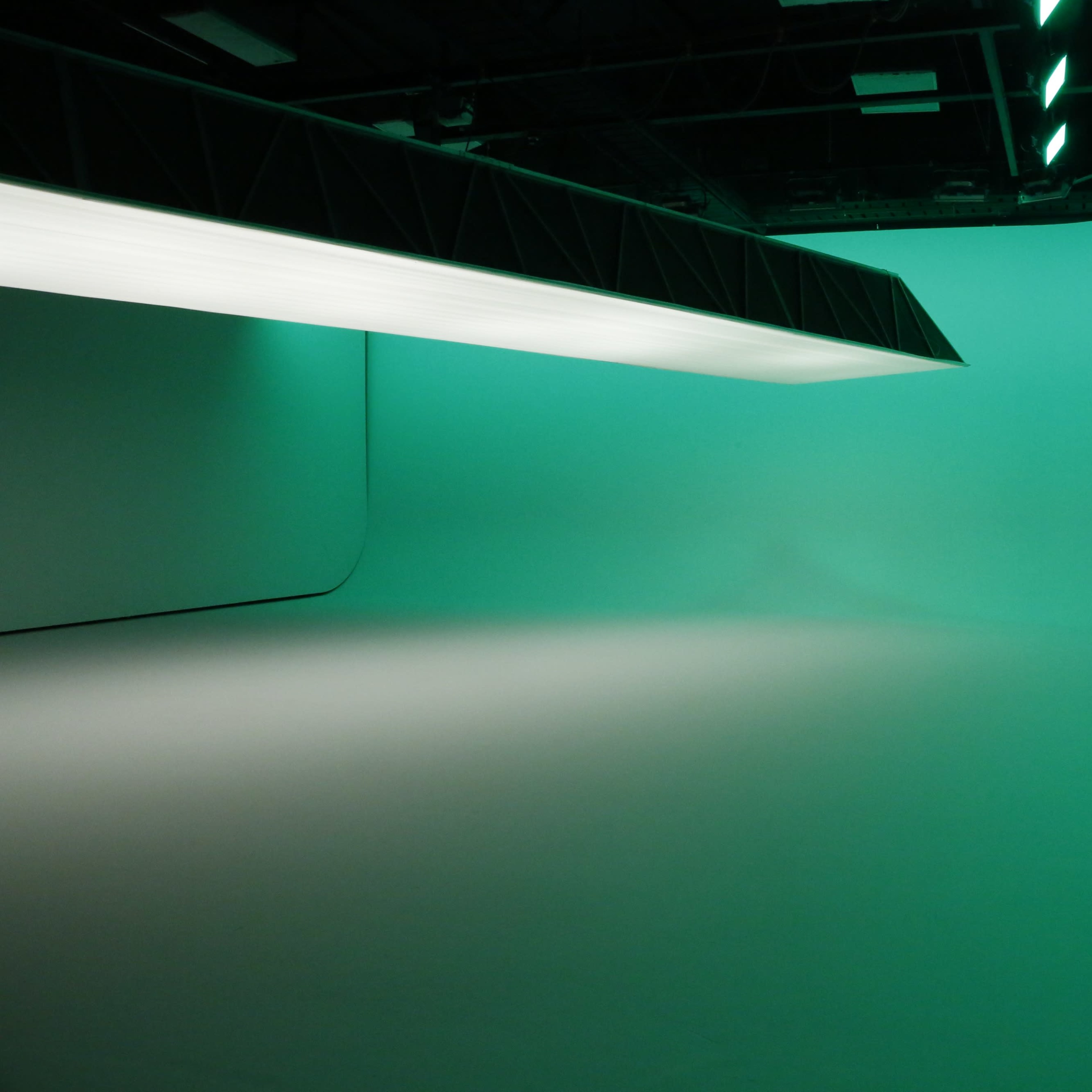 An empty studio space with a smooth, gradient backdrop illuminated in green.