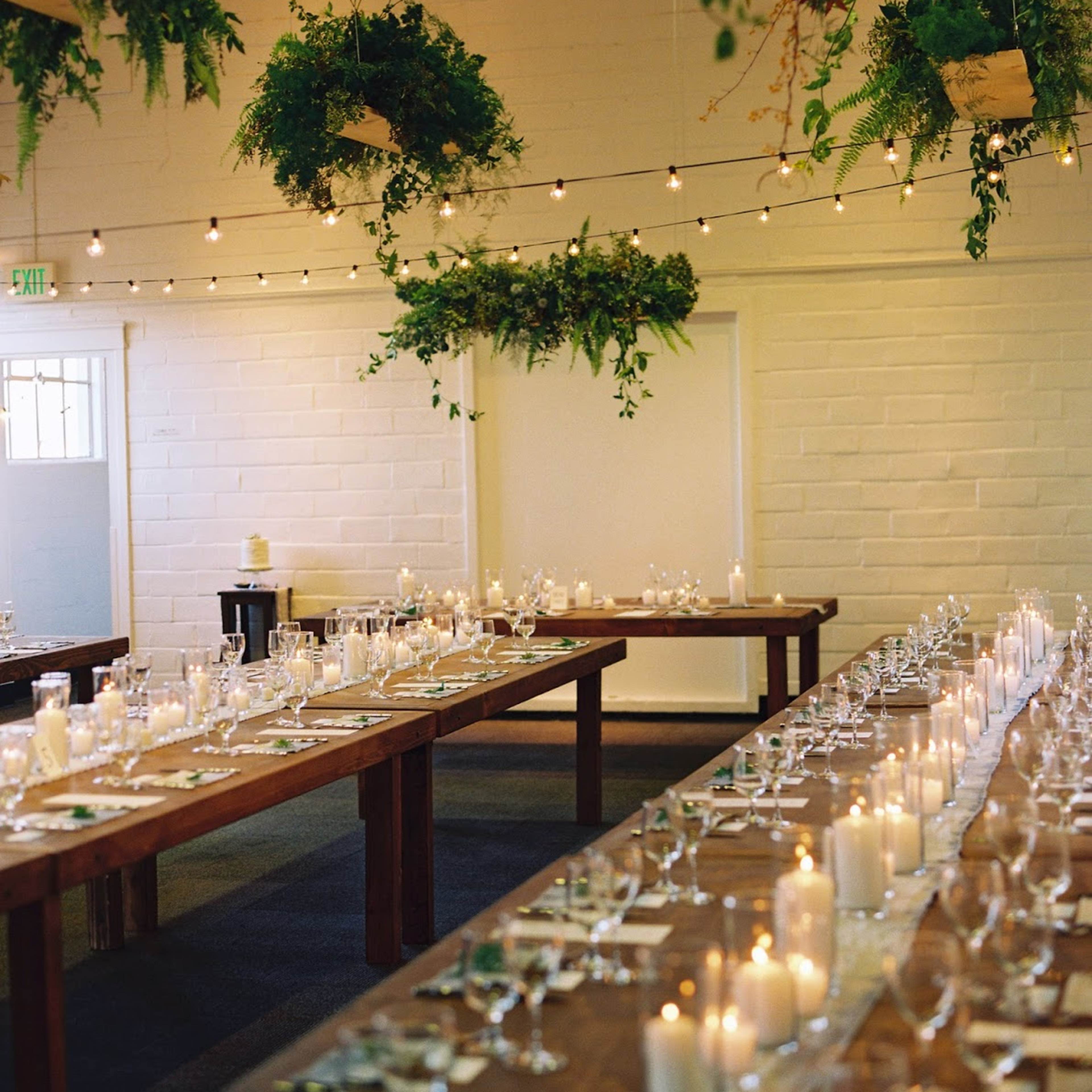 A decorated dining hall with long wooden tables set for a meal, adorned with candles and greenery hanging from the ceiling.