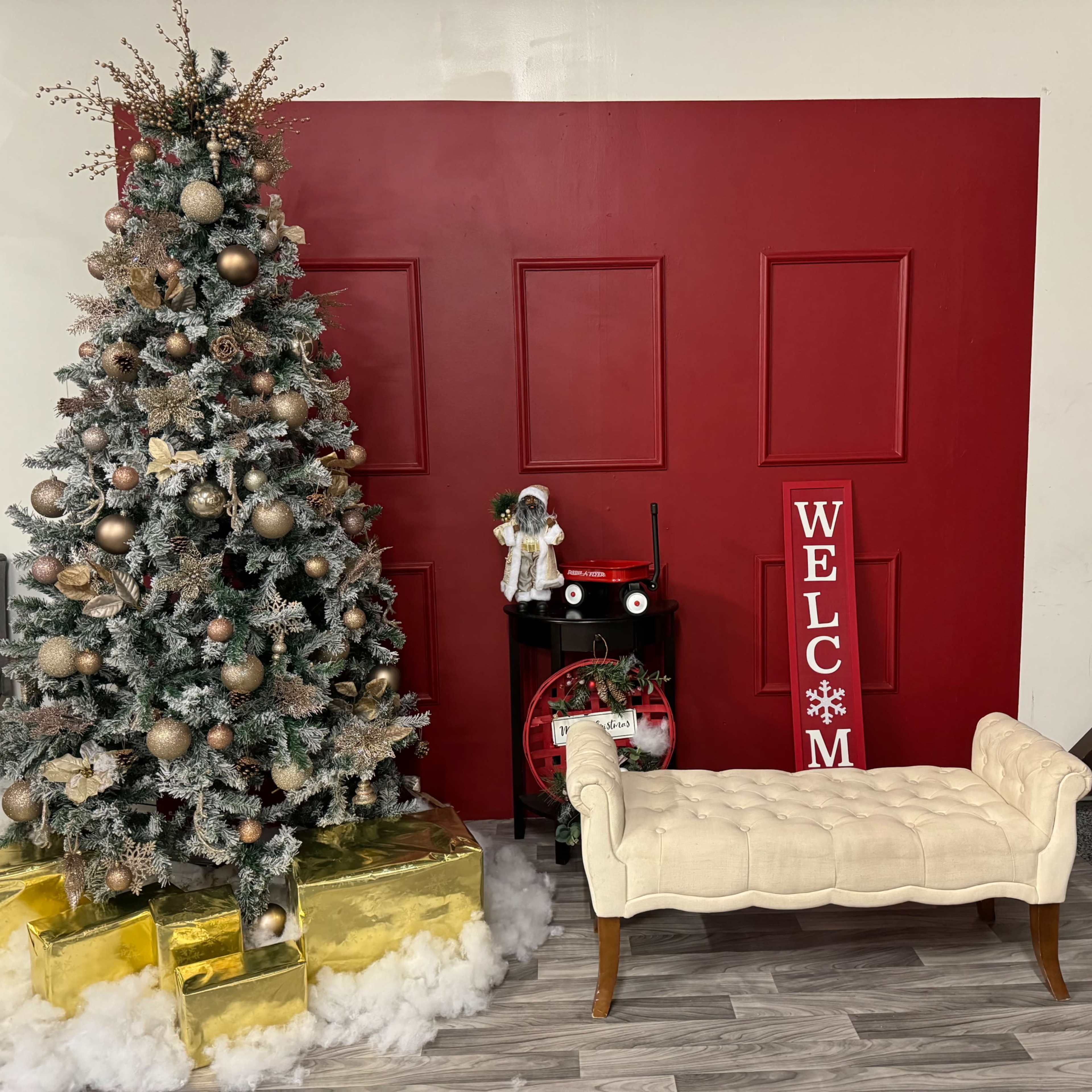 The scene features a decorated Christmas tree beside a red wall, a sign that reads "WELCOME," and a white bench in front of a vintage cart.