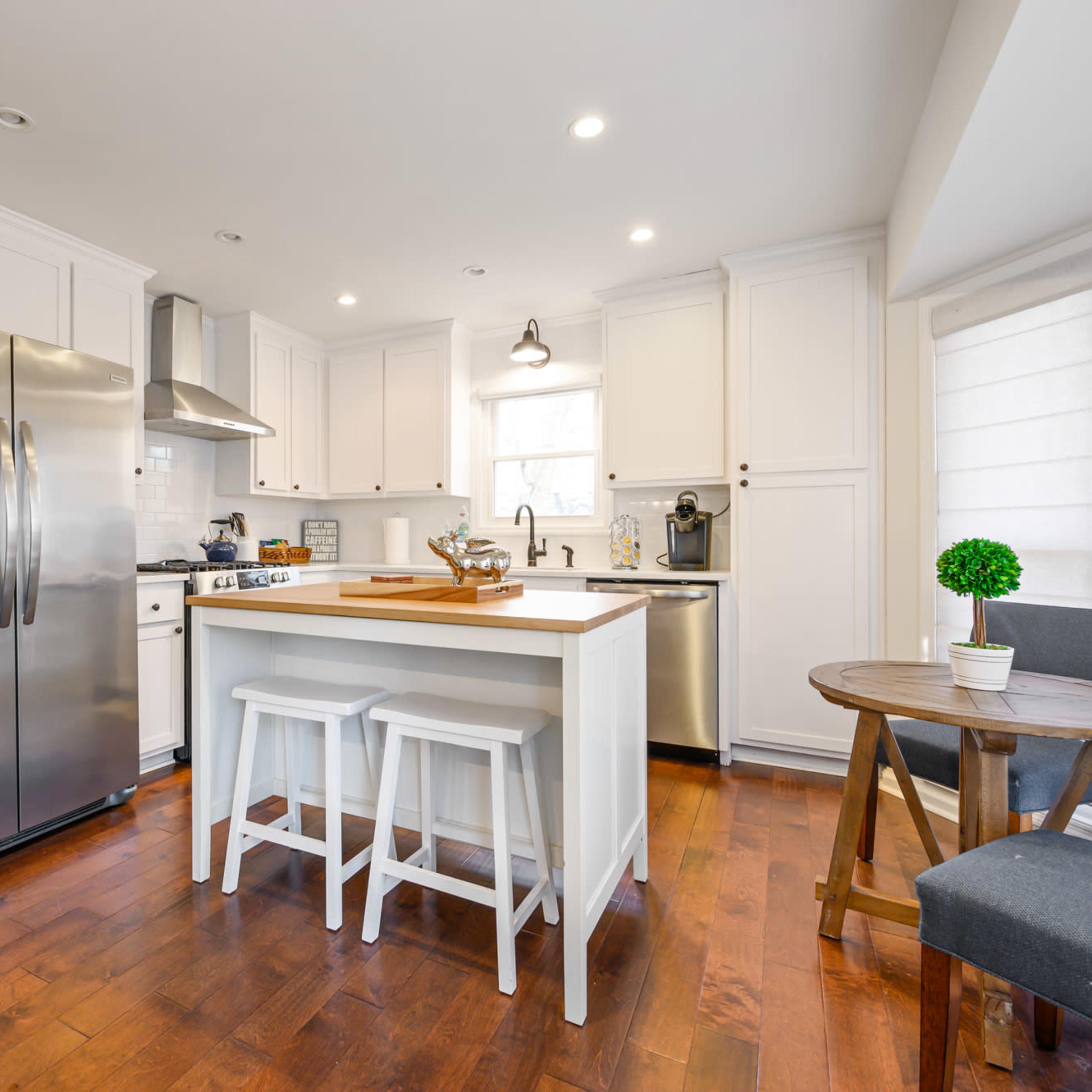 A modern kitchen features white cabinetry, stainless steel appliances, a central island with seating, and hardwood flooring.