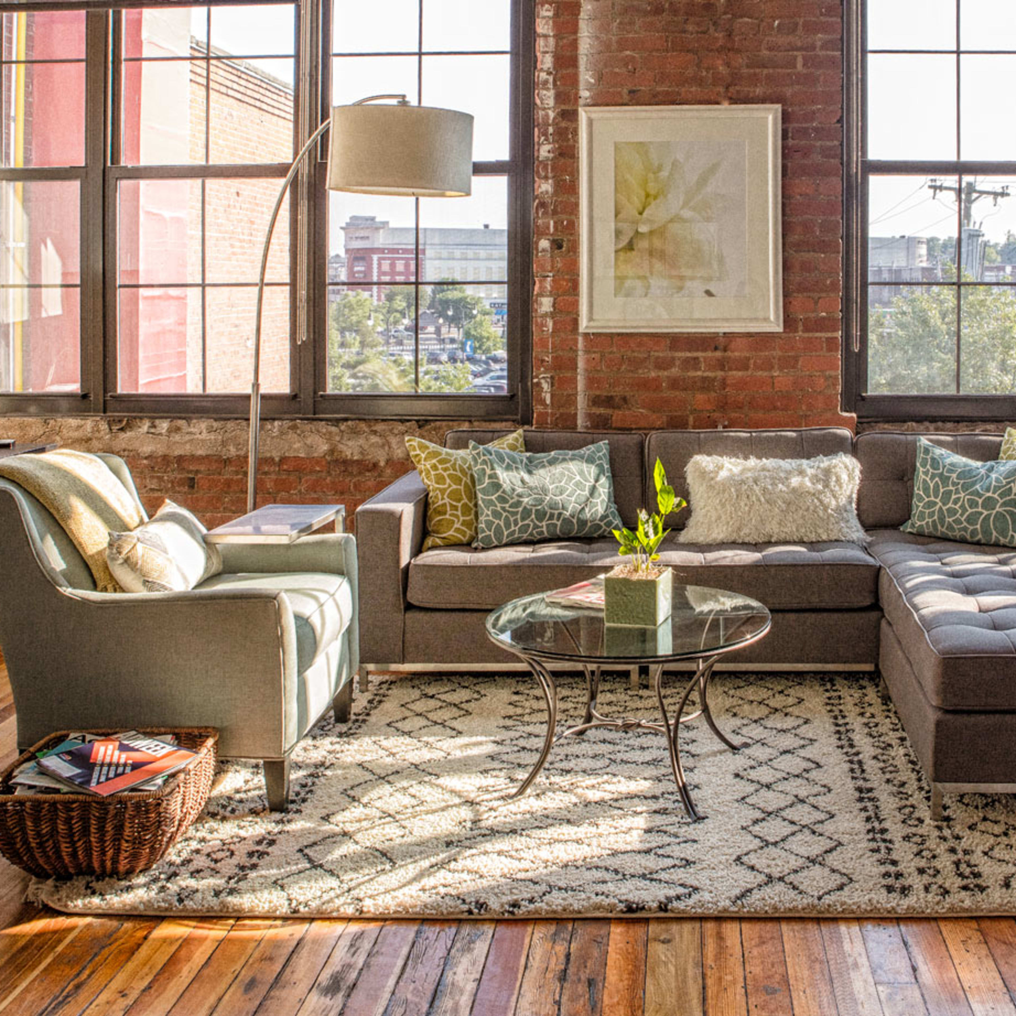 A cozy living room with a sectional sofa, a glass coffee table, and large windows allowing natural light to fill the space.