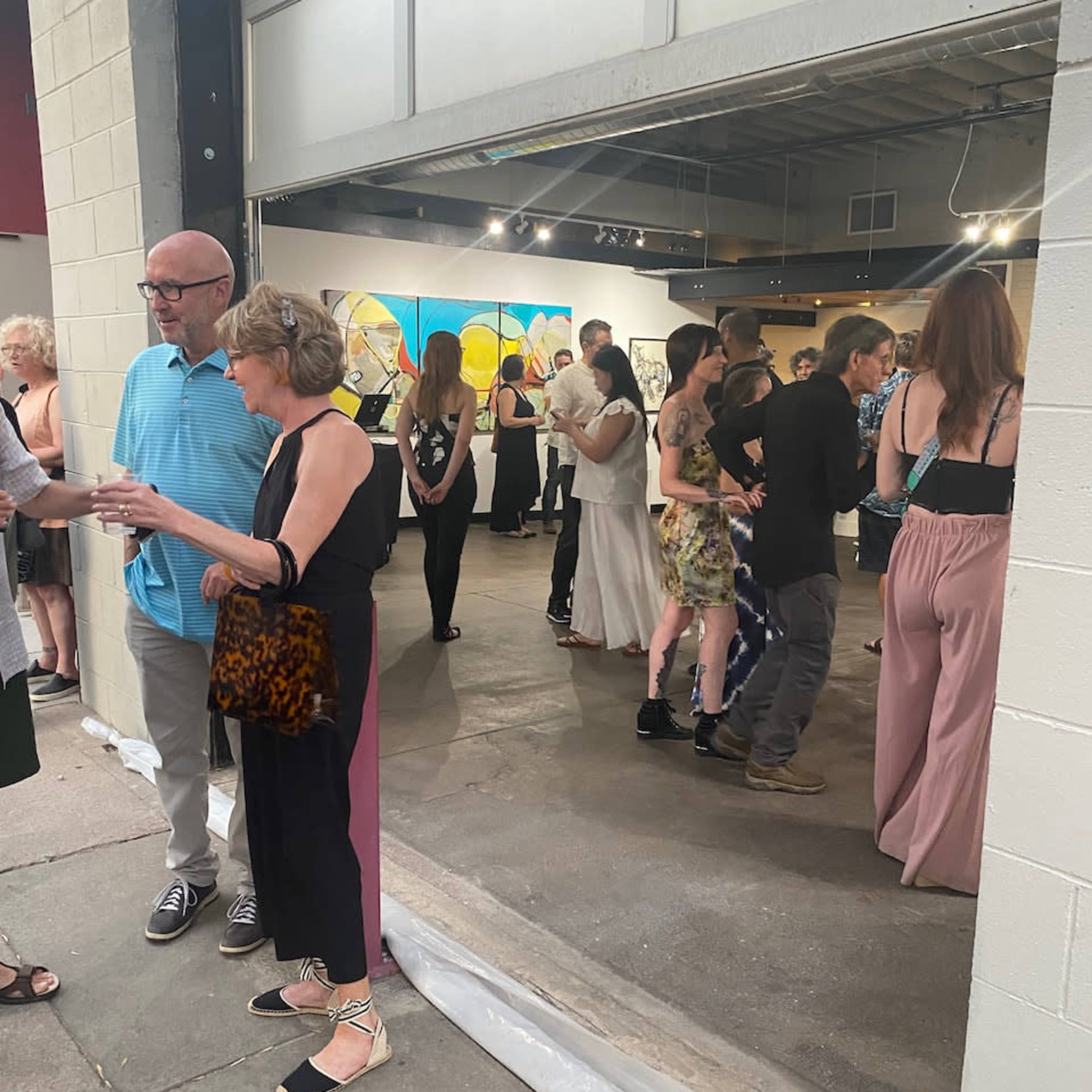 A group of people socialize inside an art gallery with colorful abstract paintings on the wall.