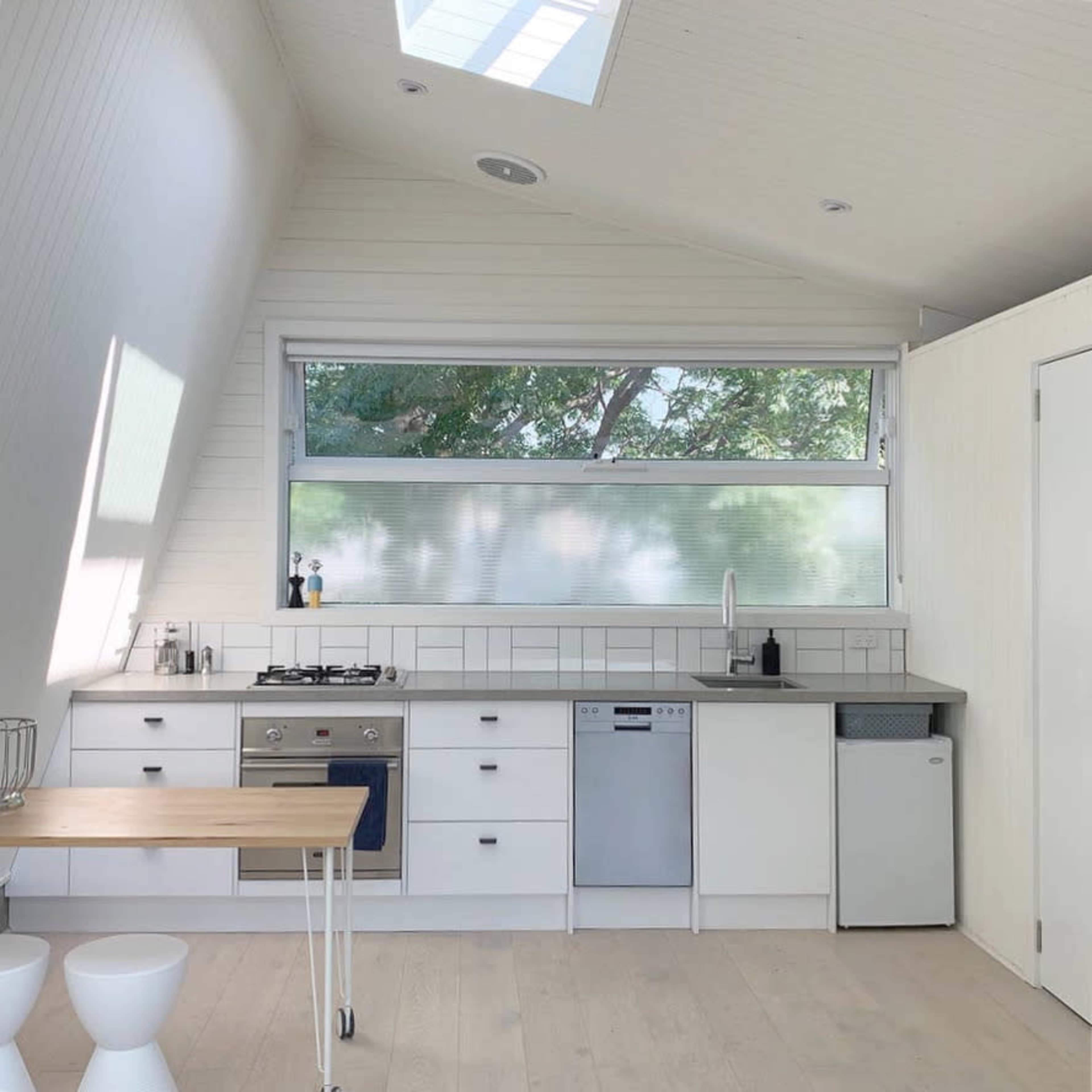 A modern kitchen with white cabinetry, a stove, a dishwasher, and a large window allowing natural light to enter.